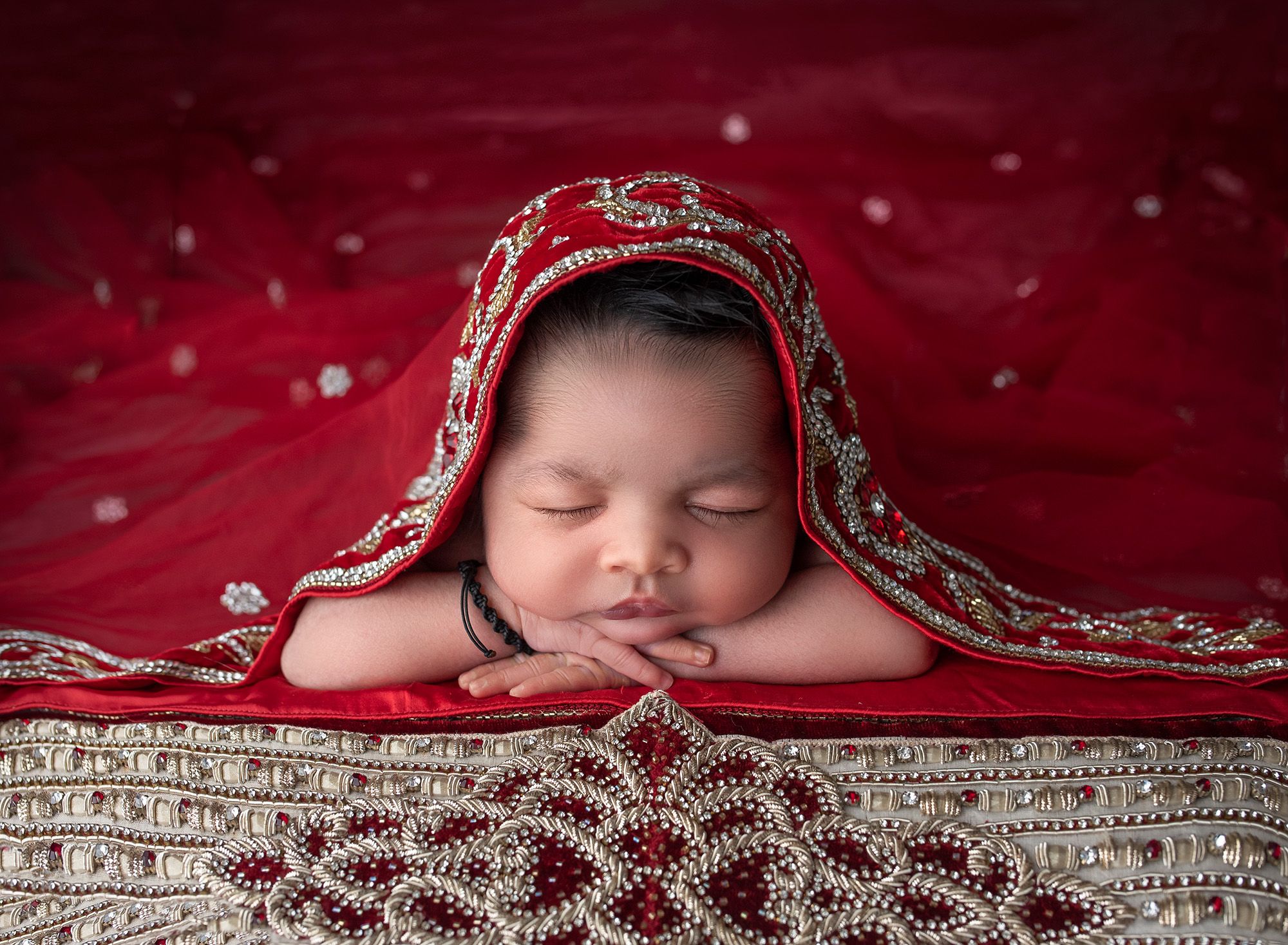 Newborn Photos full of color newborn baby girl asleep draped in red traditional costume