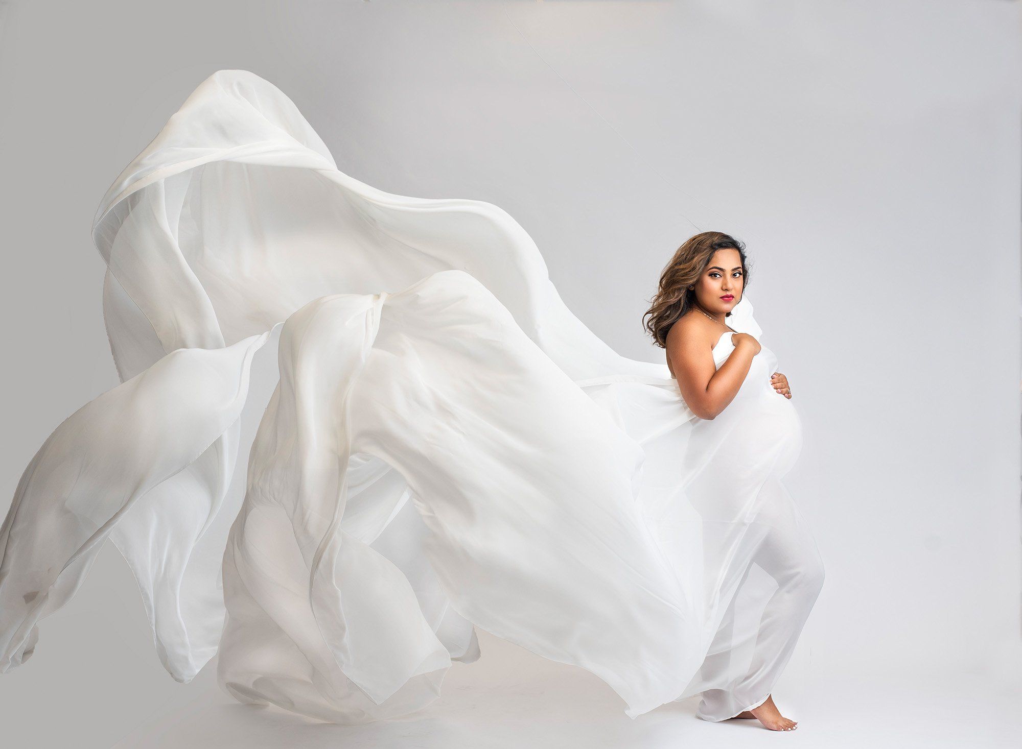 pregnant woman posing in white flowing maternity dress