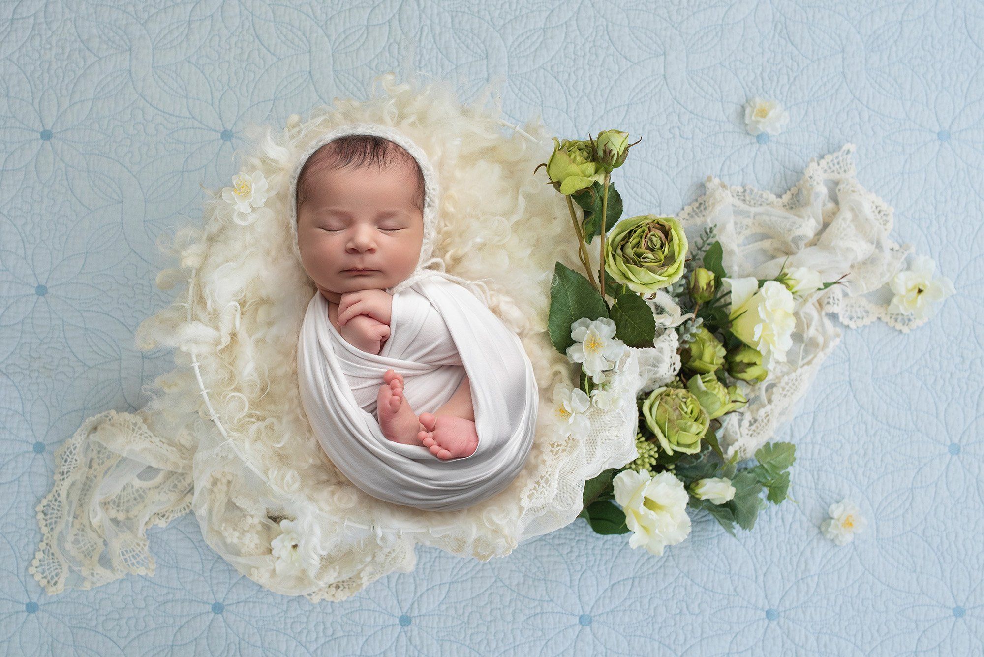 baby girl swaddled in white laying on top of antique lace blanket with white and green floral accents