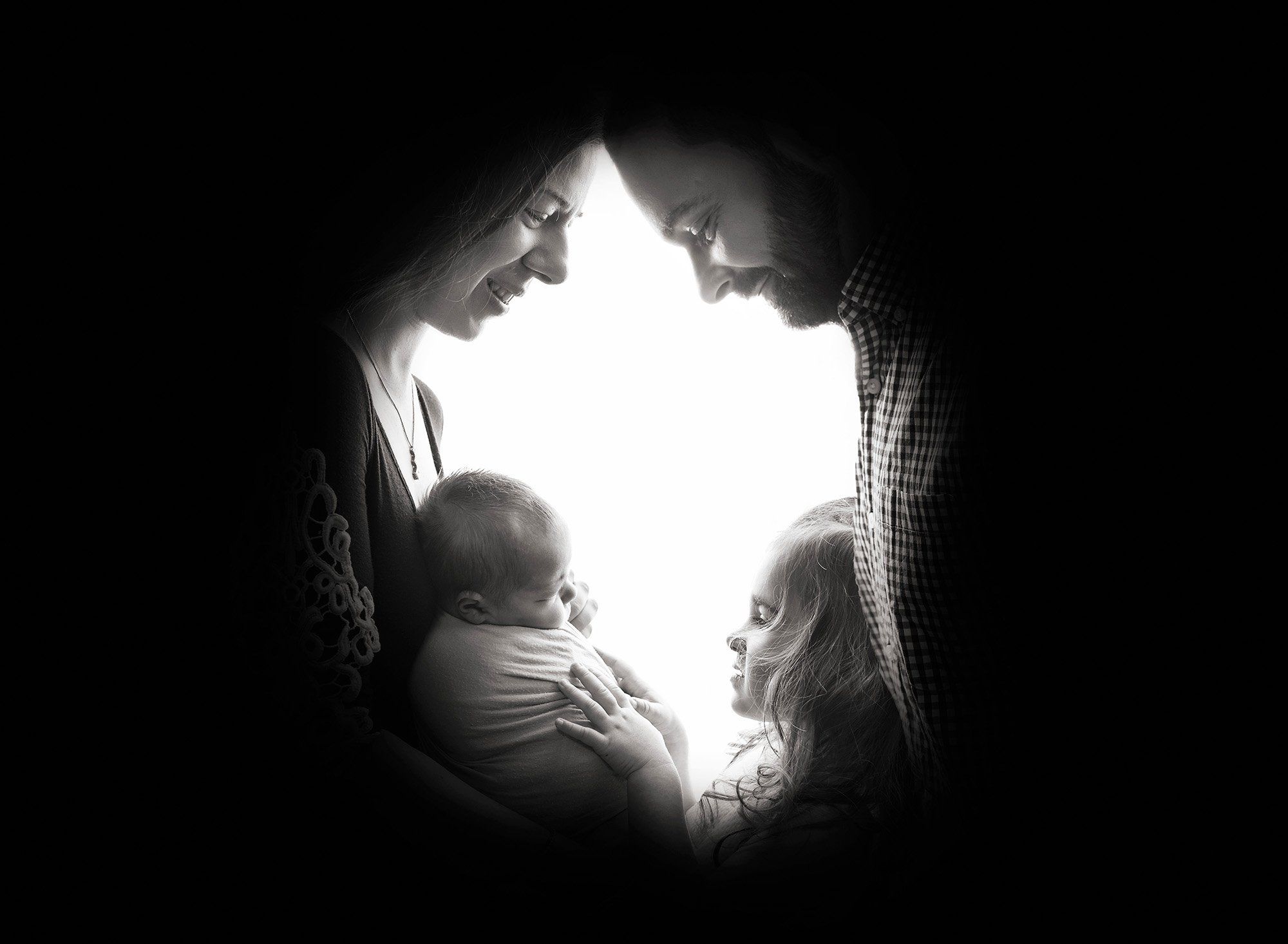 silhouette shadow of parents face's while cradling their newborn baby boy and older sister peaks in