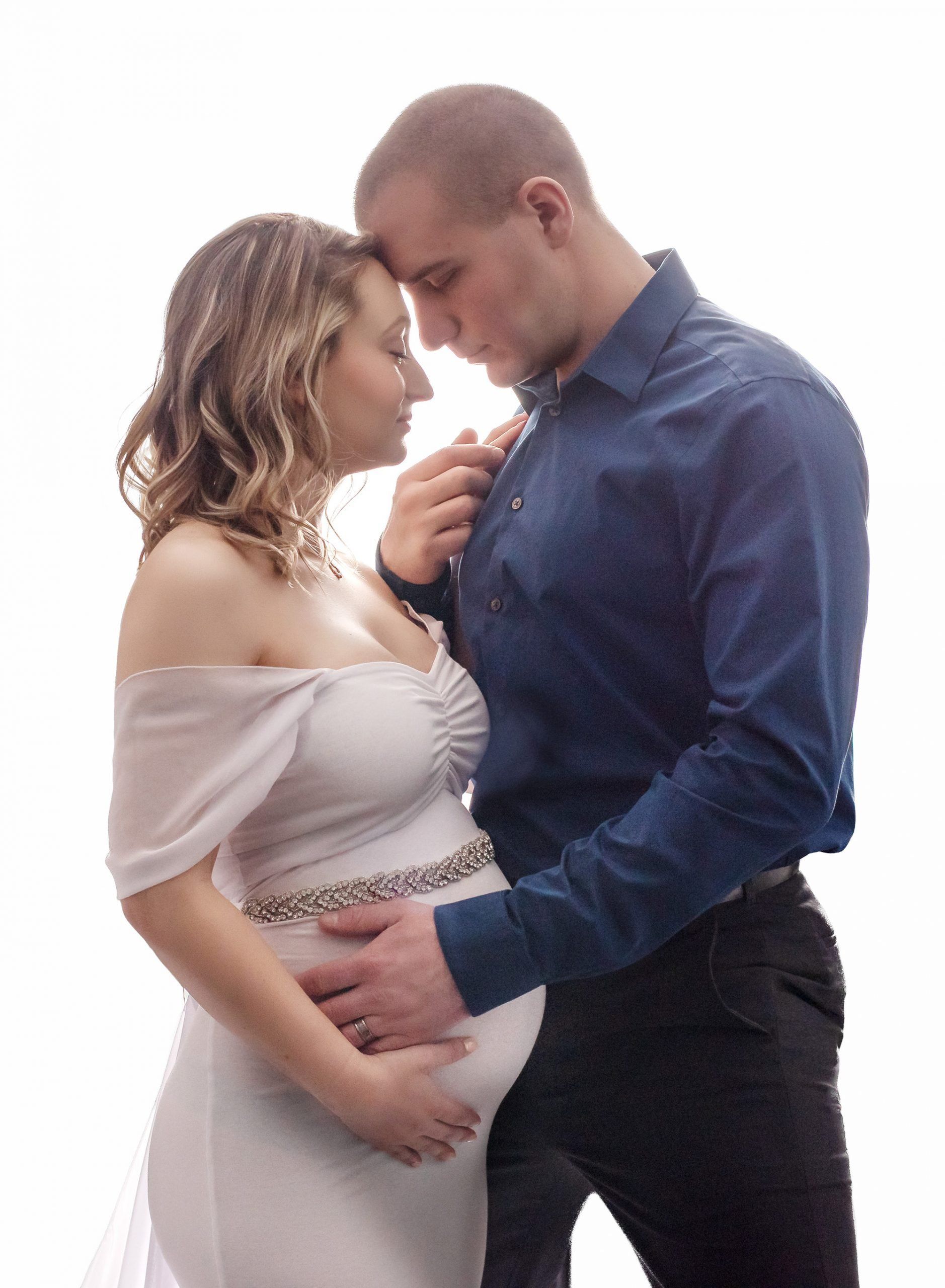partner holding pregnant womans stomach in white gown while leaning in close