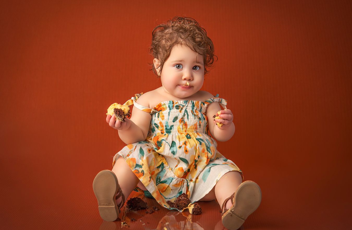 Baby Photographer CT adorable 1 year old baby girl eating cake on an orange background