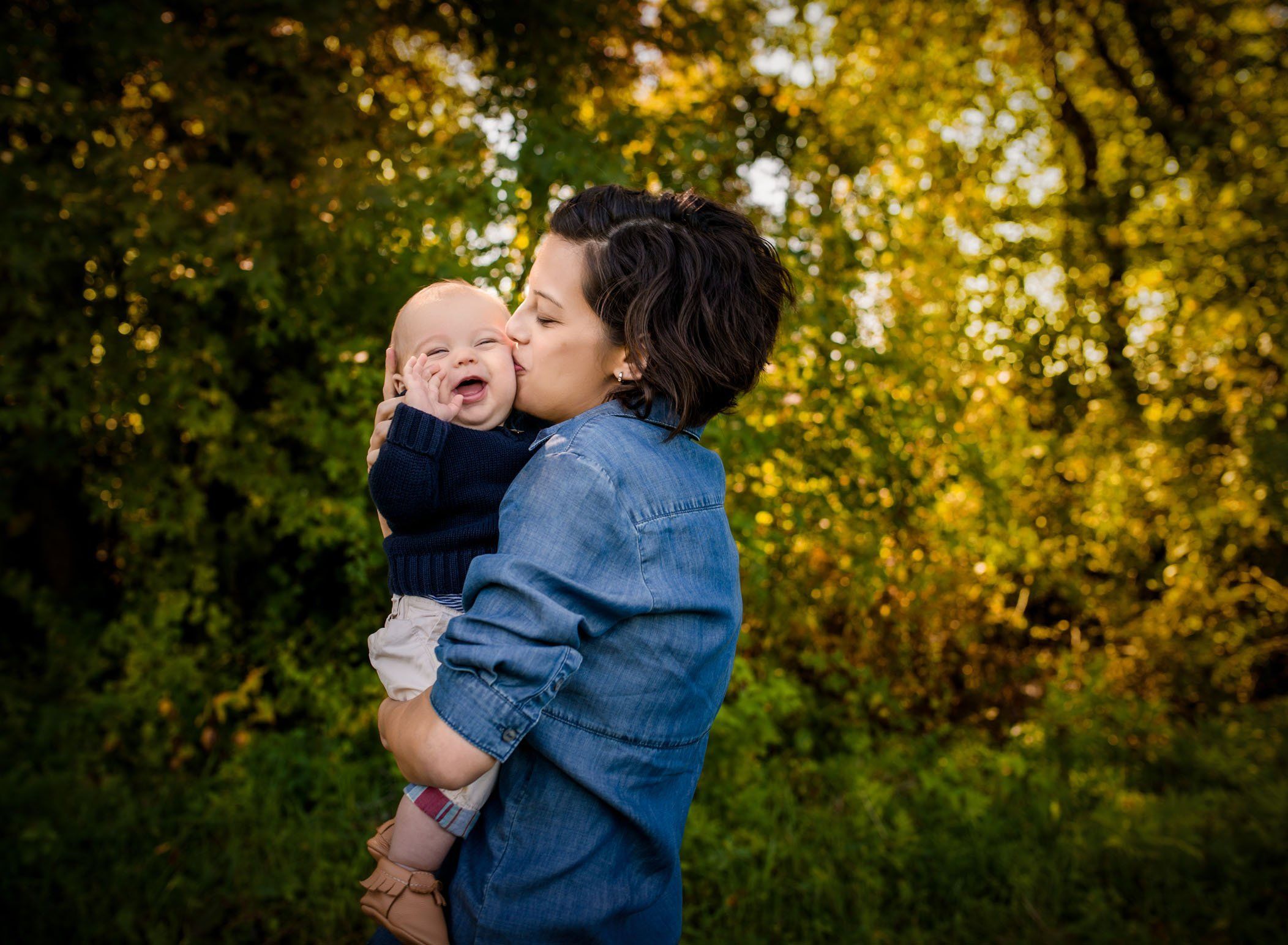 Mom kissing 6 month old baby boy outside in fall foliage