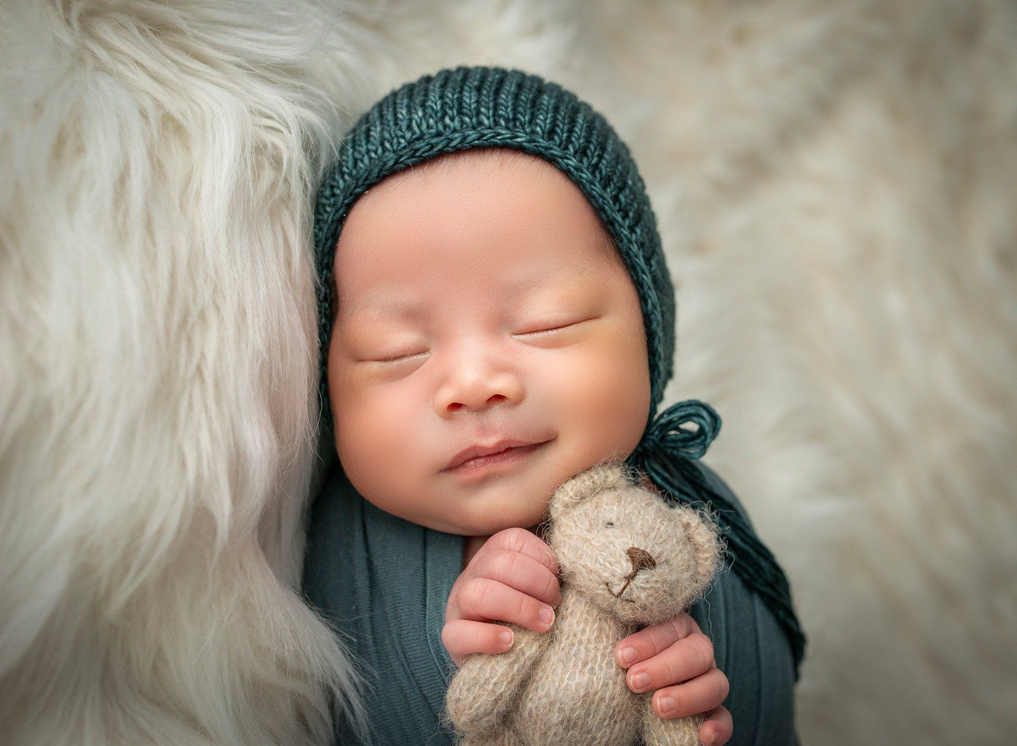 newborn baby boy asleep swaddled in green holding teddy bear on a fluffy blanket