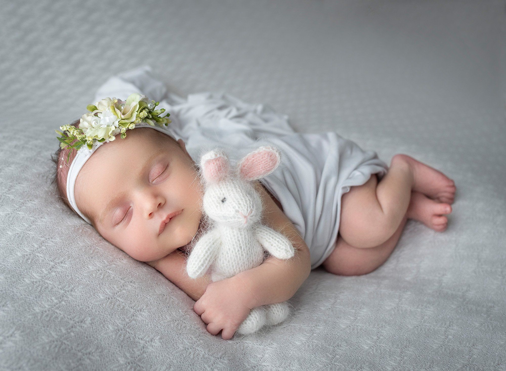 newborn baby girl asleep holding fuzzy bunny with white blanket draped over her