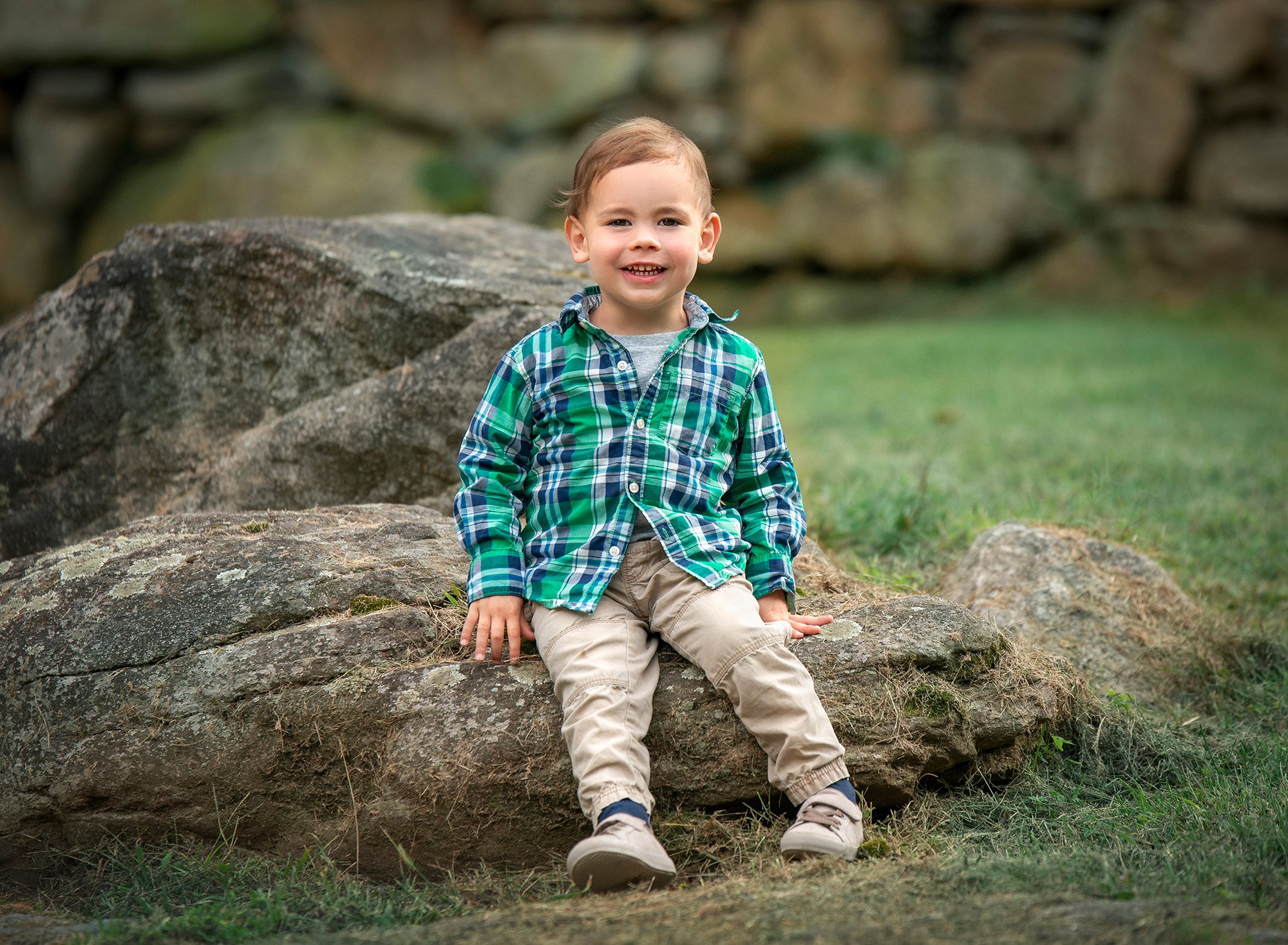 young boy in polo shirt smiling while sitting on a rock in nature