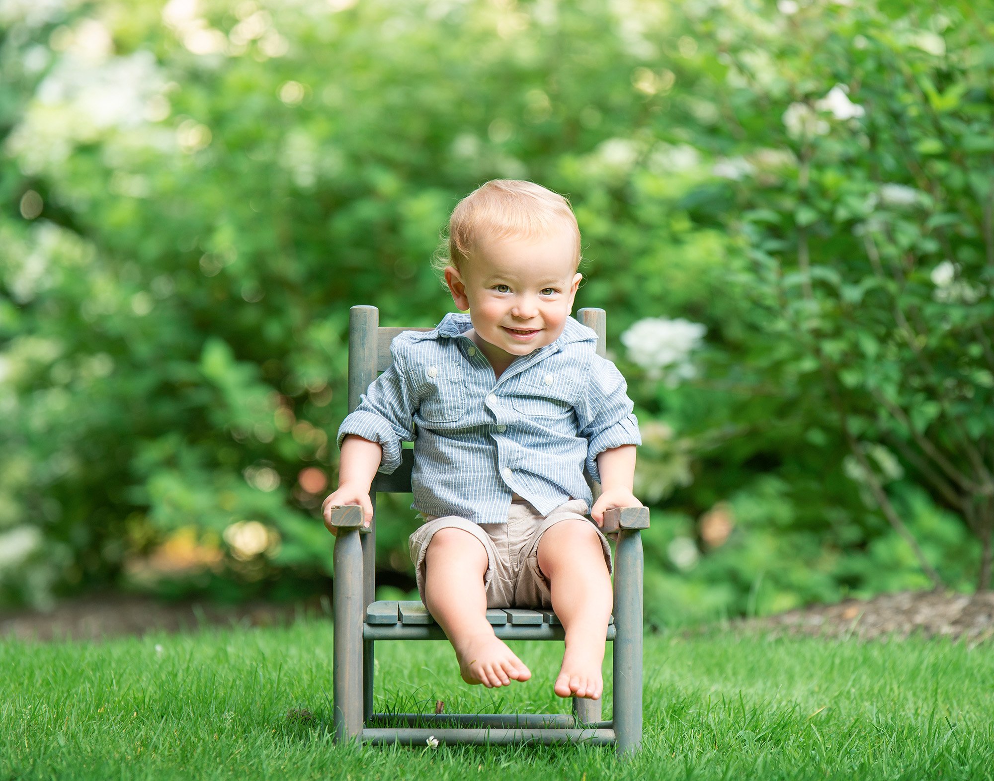 one year old boy sitting on rustic chair in nature