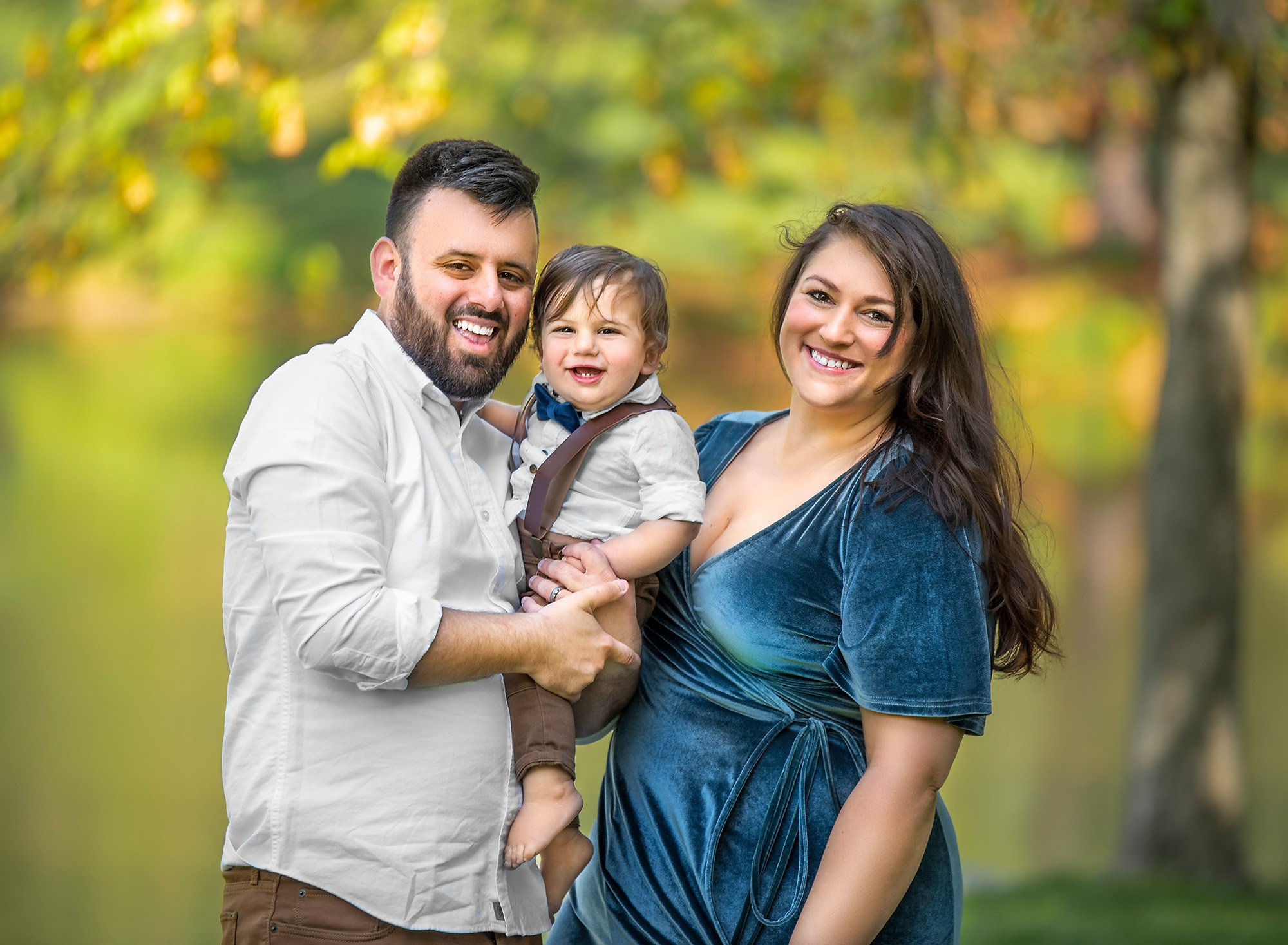 parents holding their one year old smiling boy outside