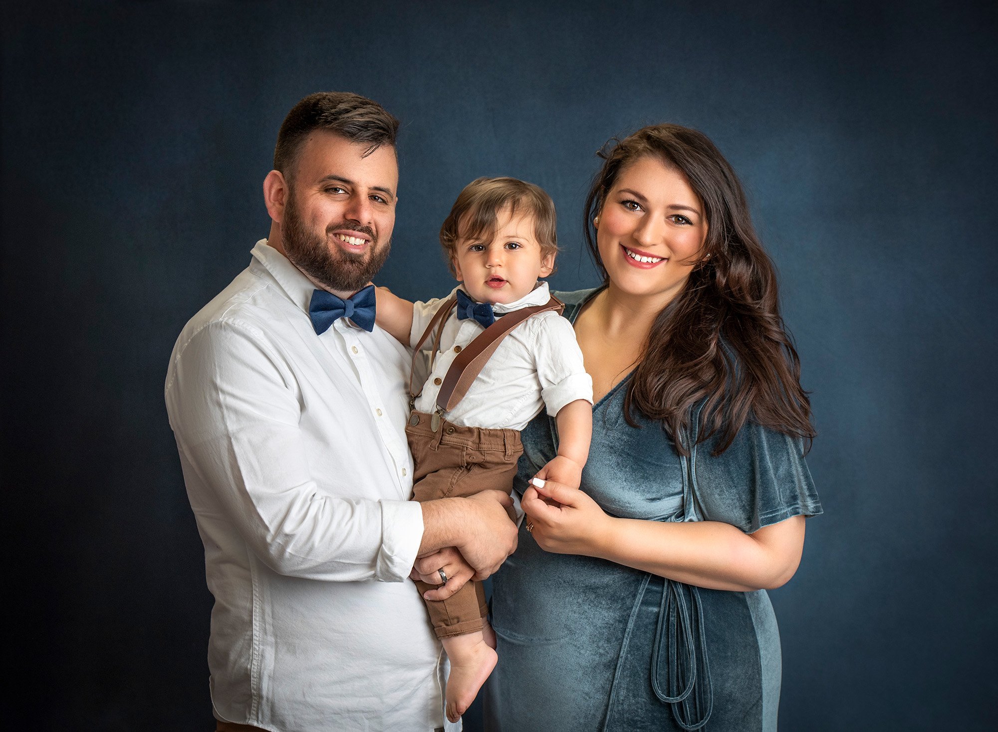 parents dressed in blue holding one year old boy wearing overalls
