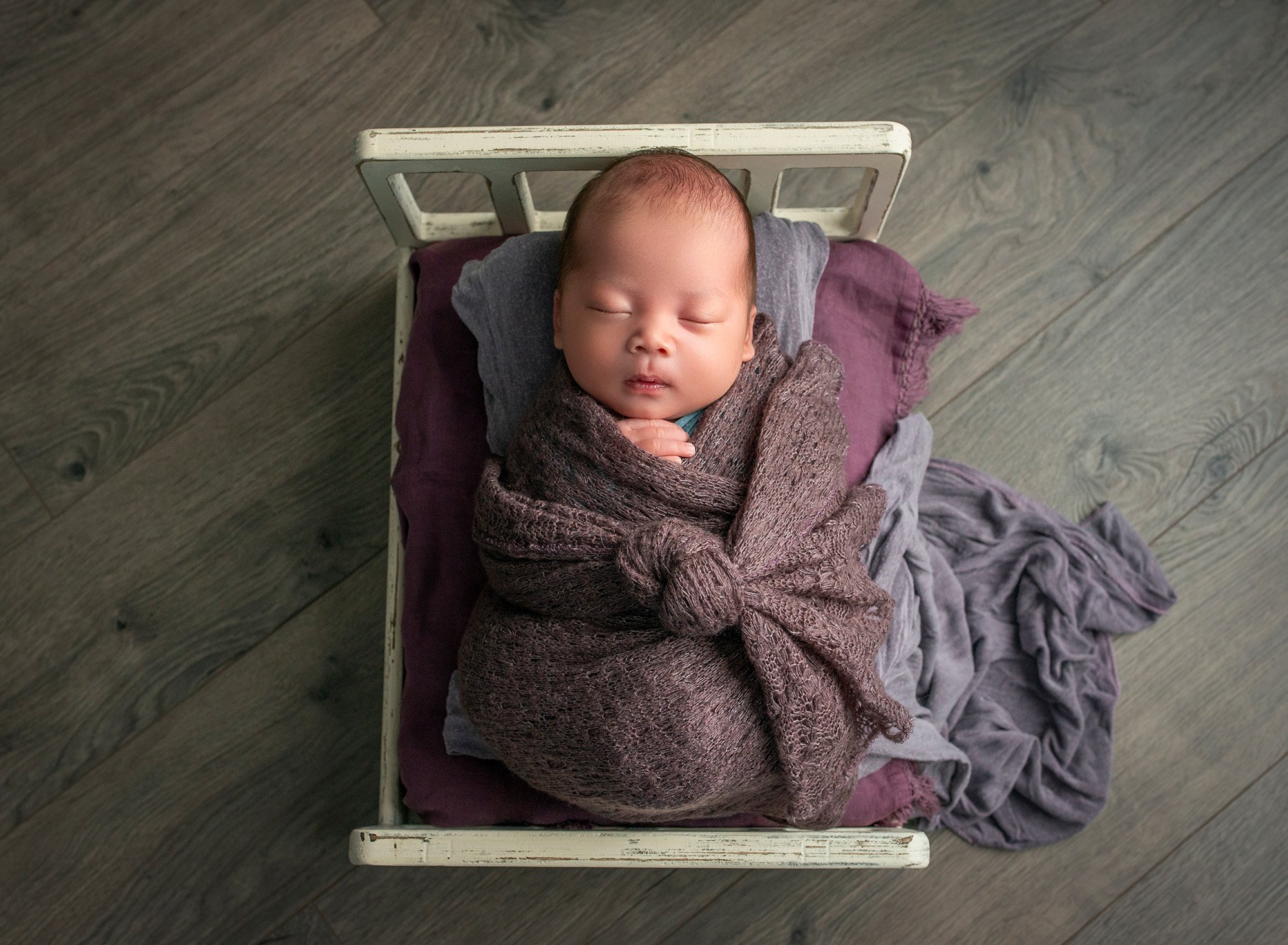Sleepy Newborn Photos newborn baby boy bundled in purple sleeping on miniature rustic white bed
