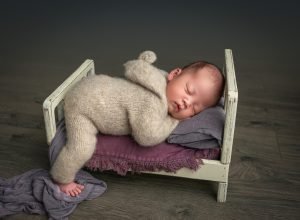Sleepy Newborn Photos baby boy asleep wearing sweater romper on miniature white rustic bed with purple blankets