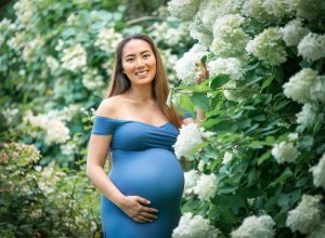 pregnant woman posing in blue dress with her hand on her stomach while holding white flowers