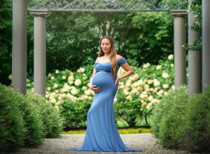 pregnant woman in blue dress posing in a flower garden