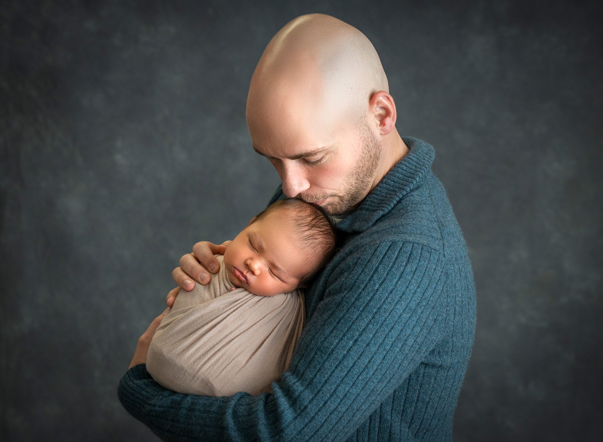 father holding newborn son, kissing his head gently