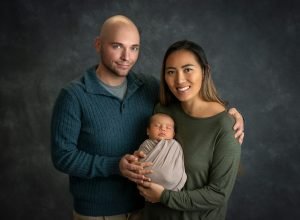 couple posing holding newborn baby boy swaddled in taupe