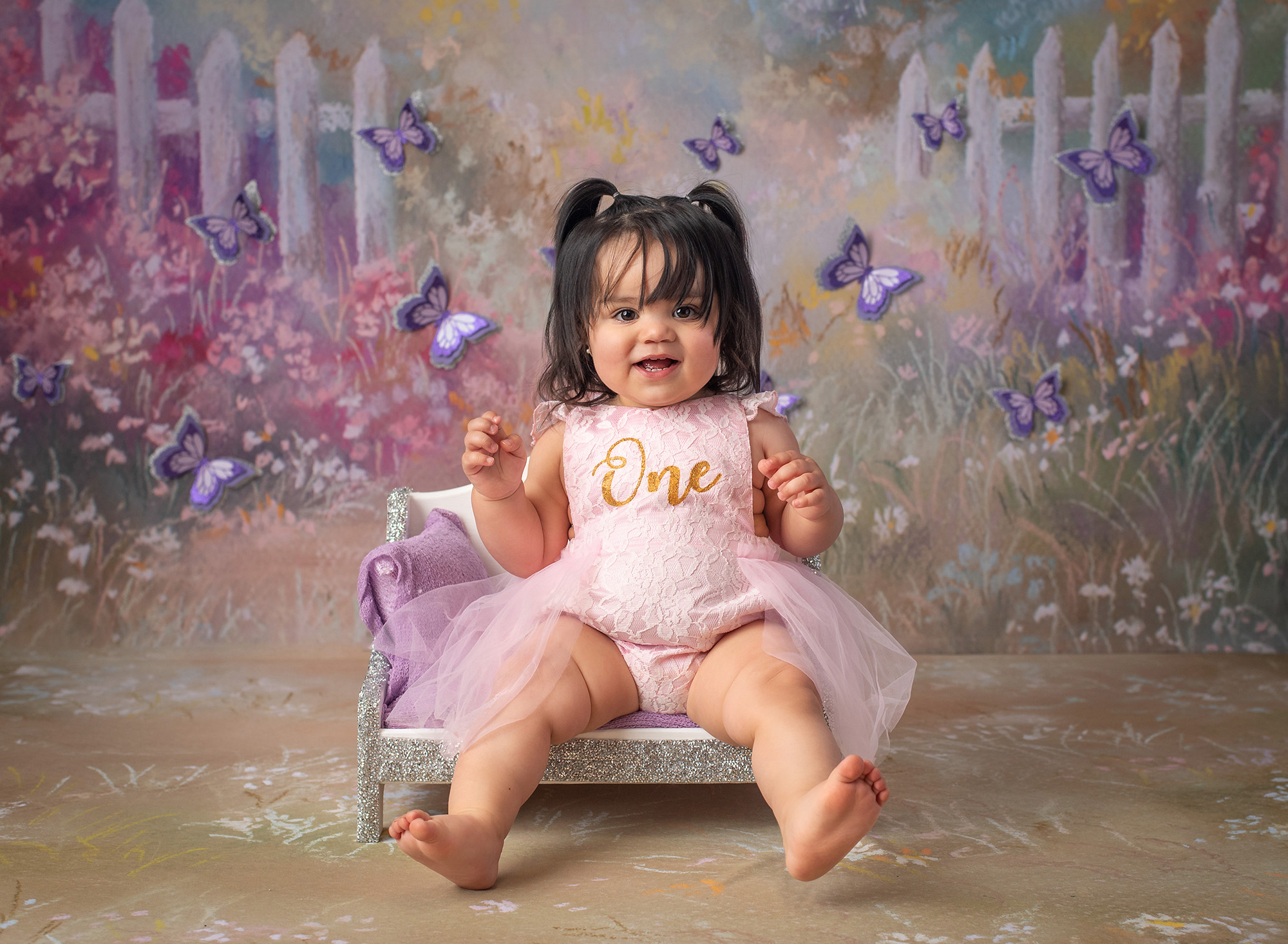 Butterfly Cake Smash Pictures one year old baby girl in pigtails dressed in pink laced dress with butterfly background