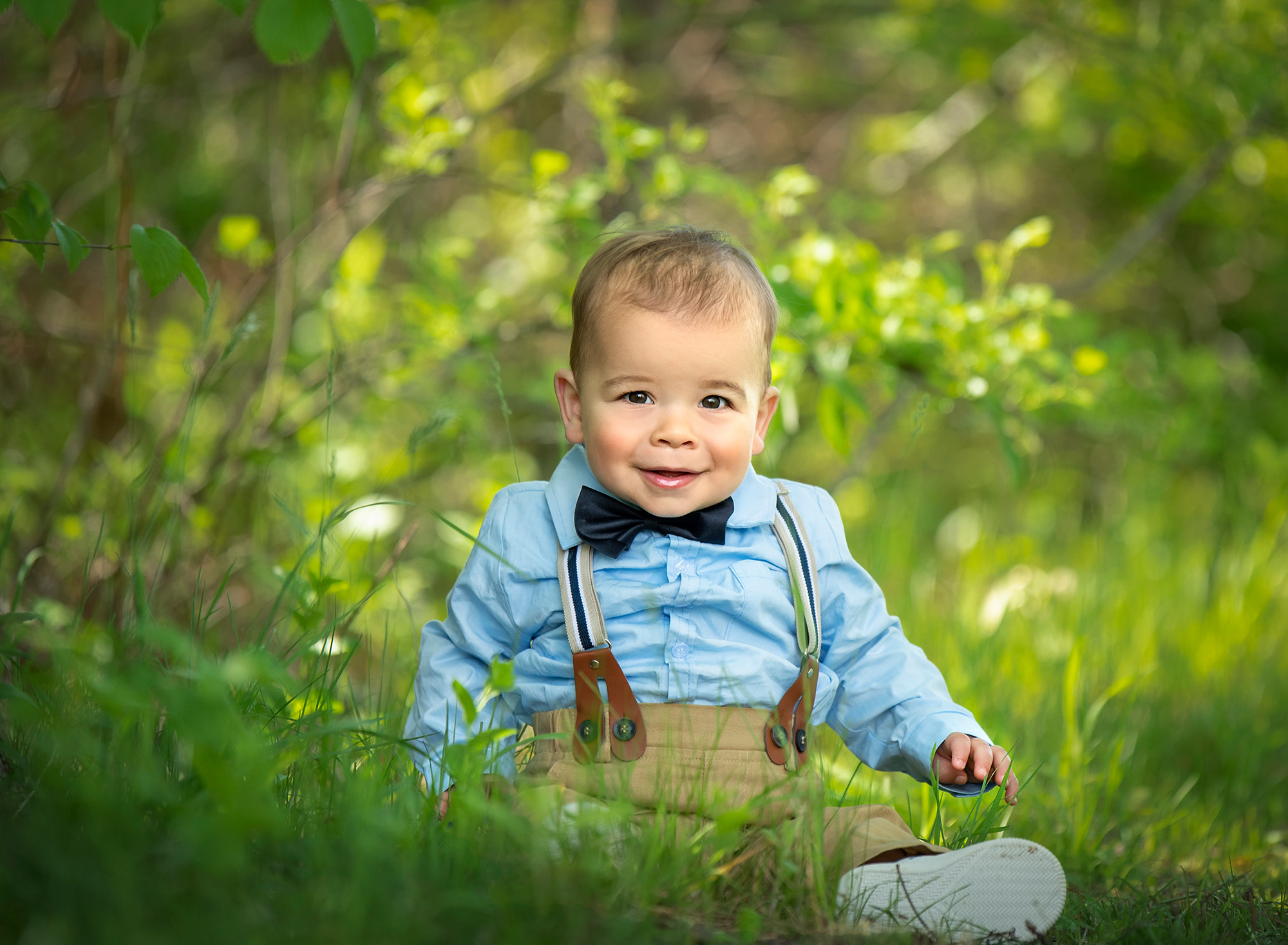 Summer Family Photos infant boy sitting on the grass smiling wearing a bow tie and suspenders