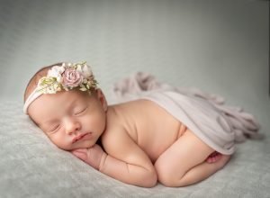 newborn baby girl laying naked with floral headband on white blanket