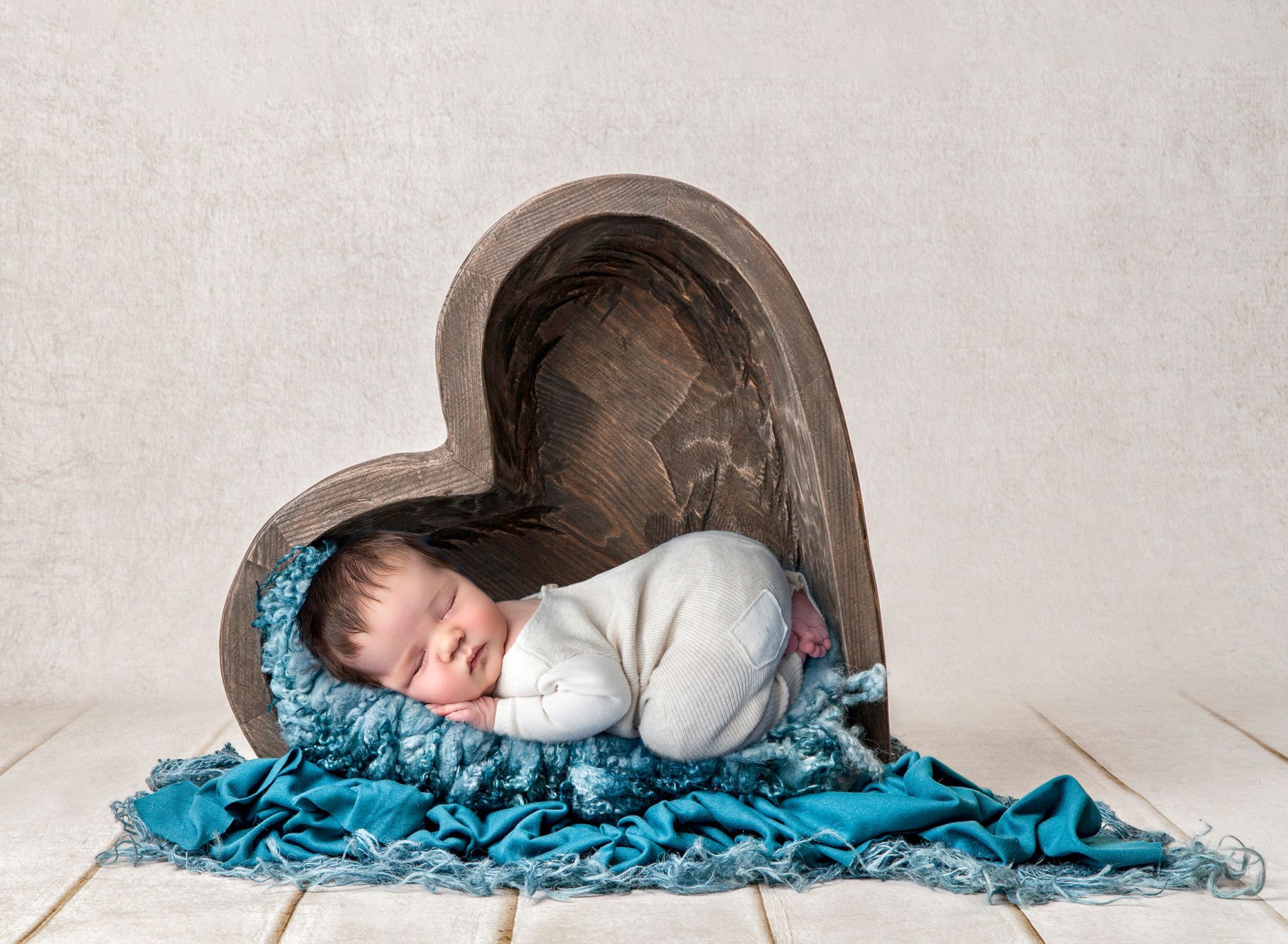newborn baby boy asleep on blue fluffy blanket inside wooden heart