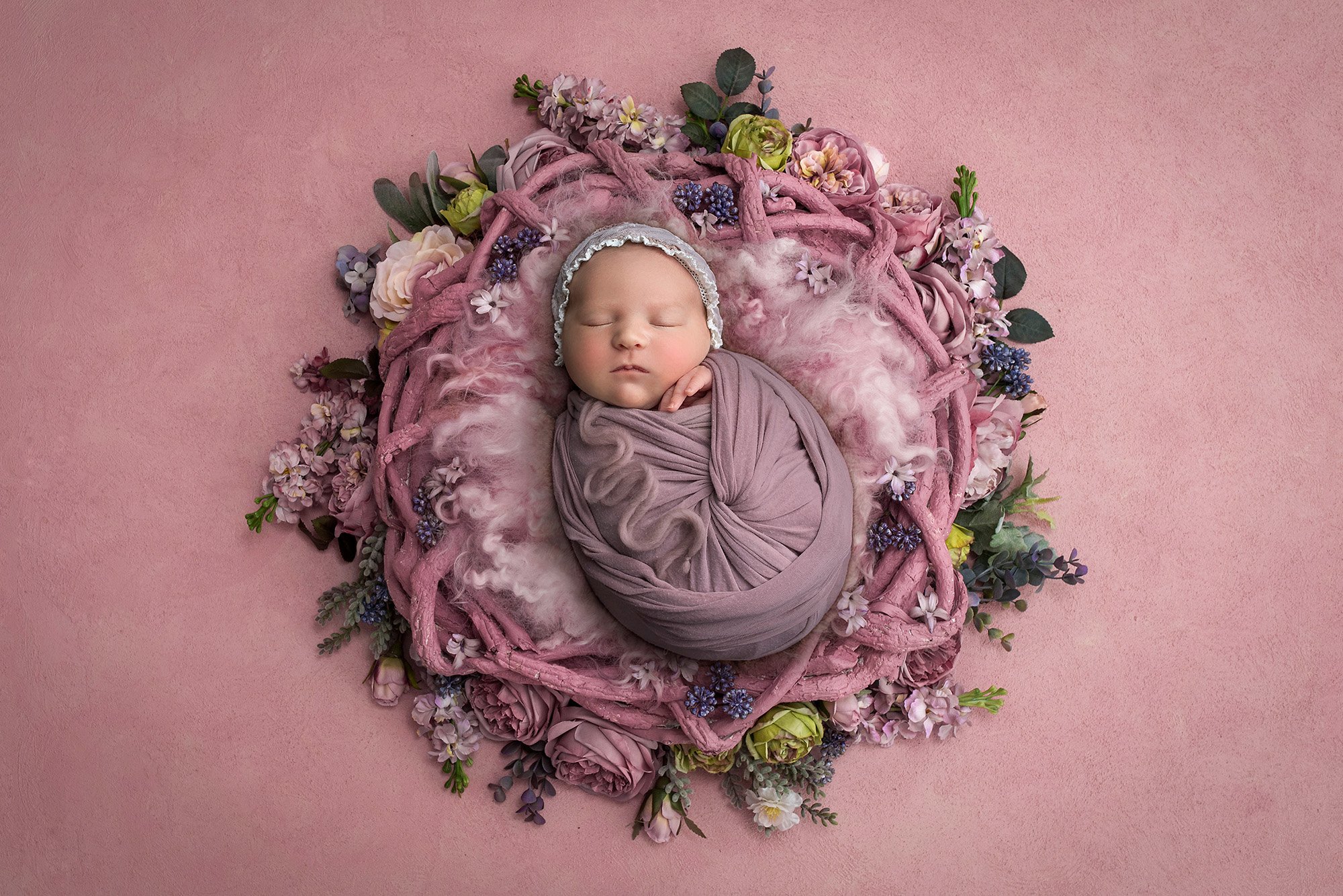swaddled newborn pictures newborn baby girl asleep in lavender wrap laying on a purple floral wreath on pink background