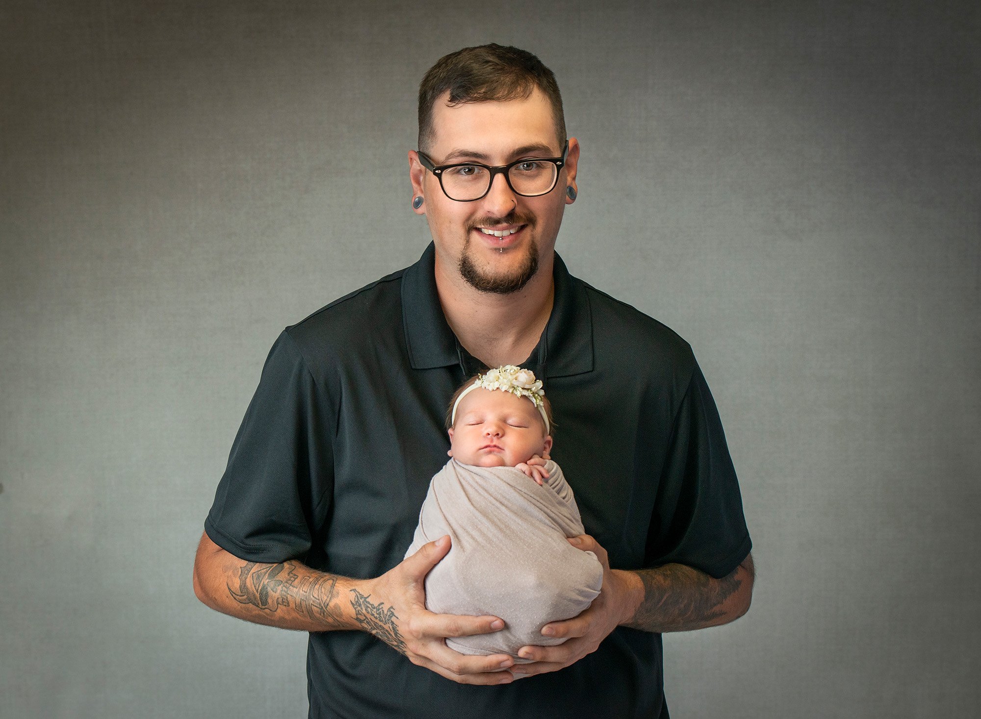 dad smiling while holding newborn baby girl swaddled in grey wrap