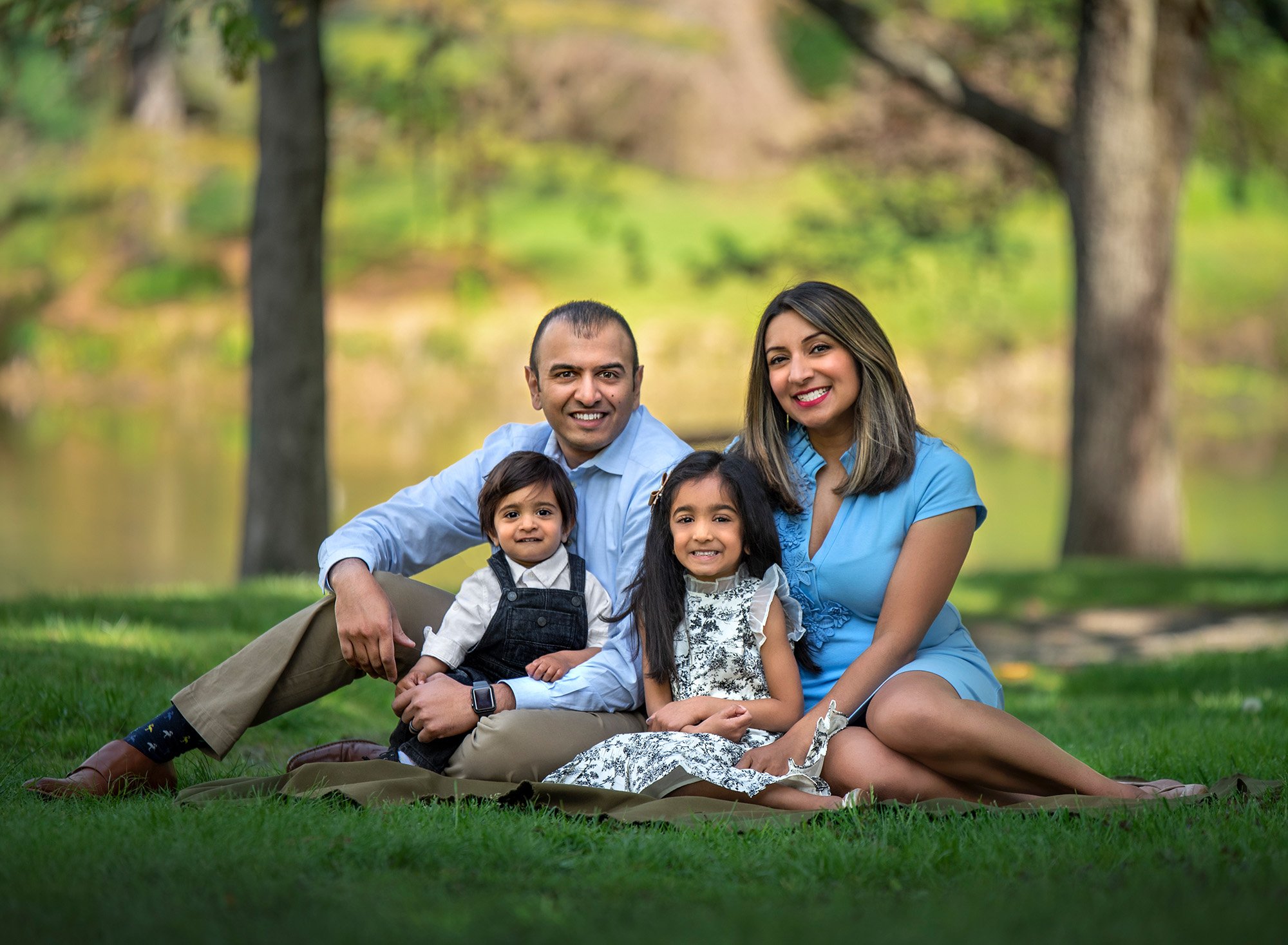 Springtime One Year Photos couple smiling sitting outside with daughter and son with trees in the background