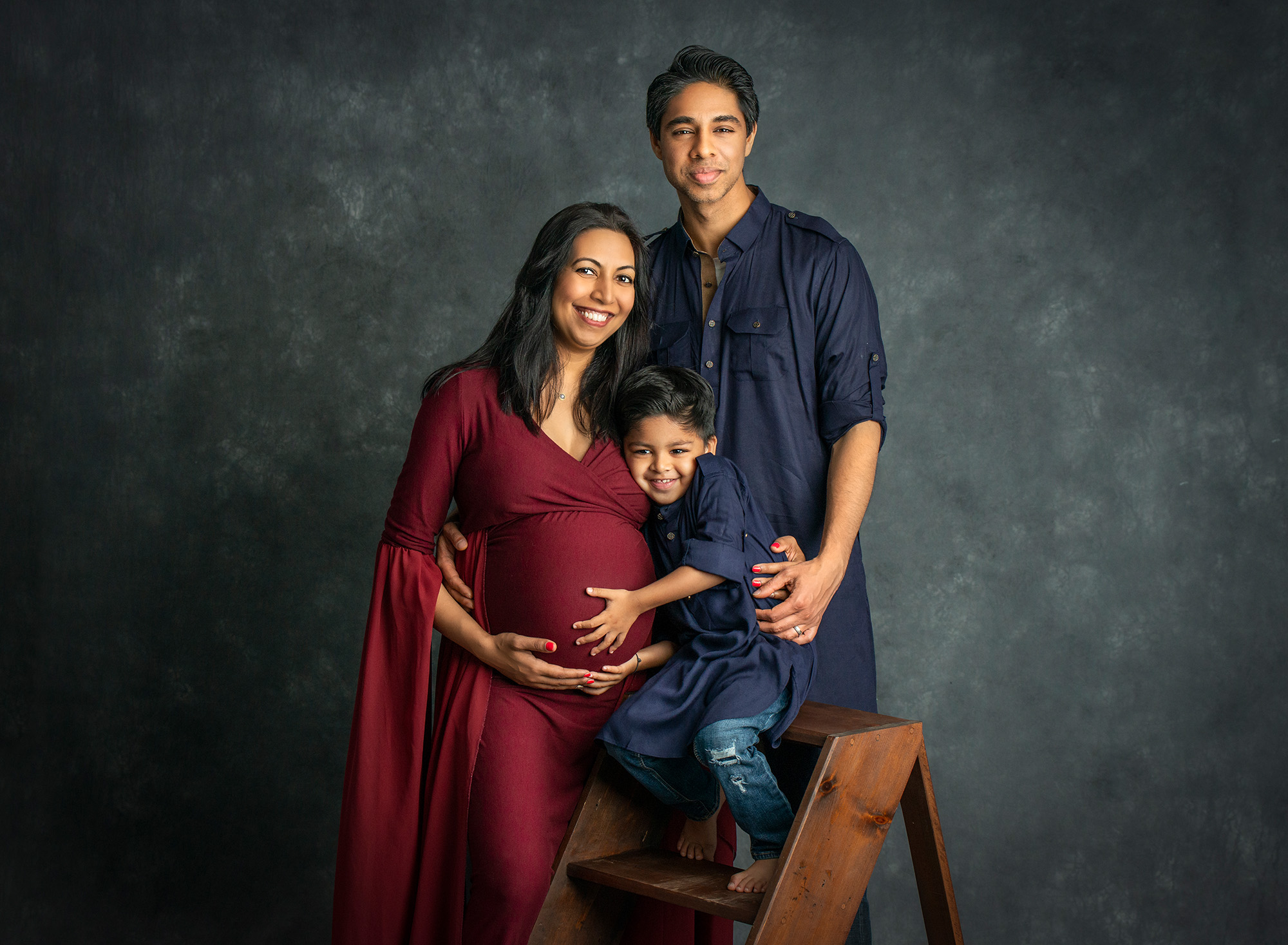 Family Maternity Photos young boy smiling while touching his mothers pregnant stomach while posing with dad