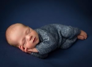 newborn baby boy asleep on his side in blue sweater romper