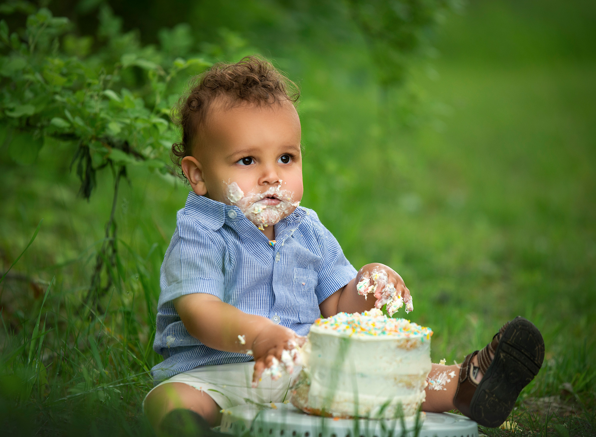 curly haired one year old boy eating cake