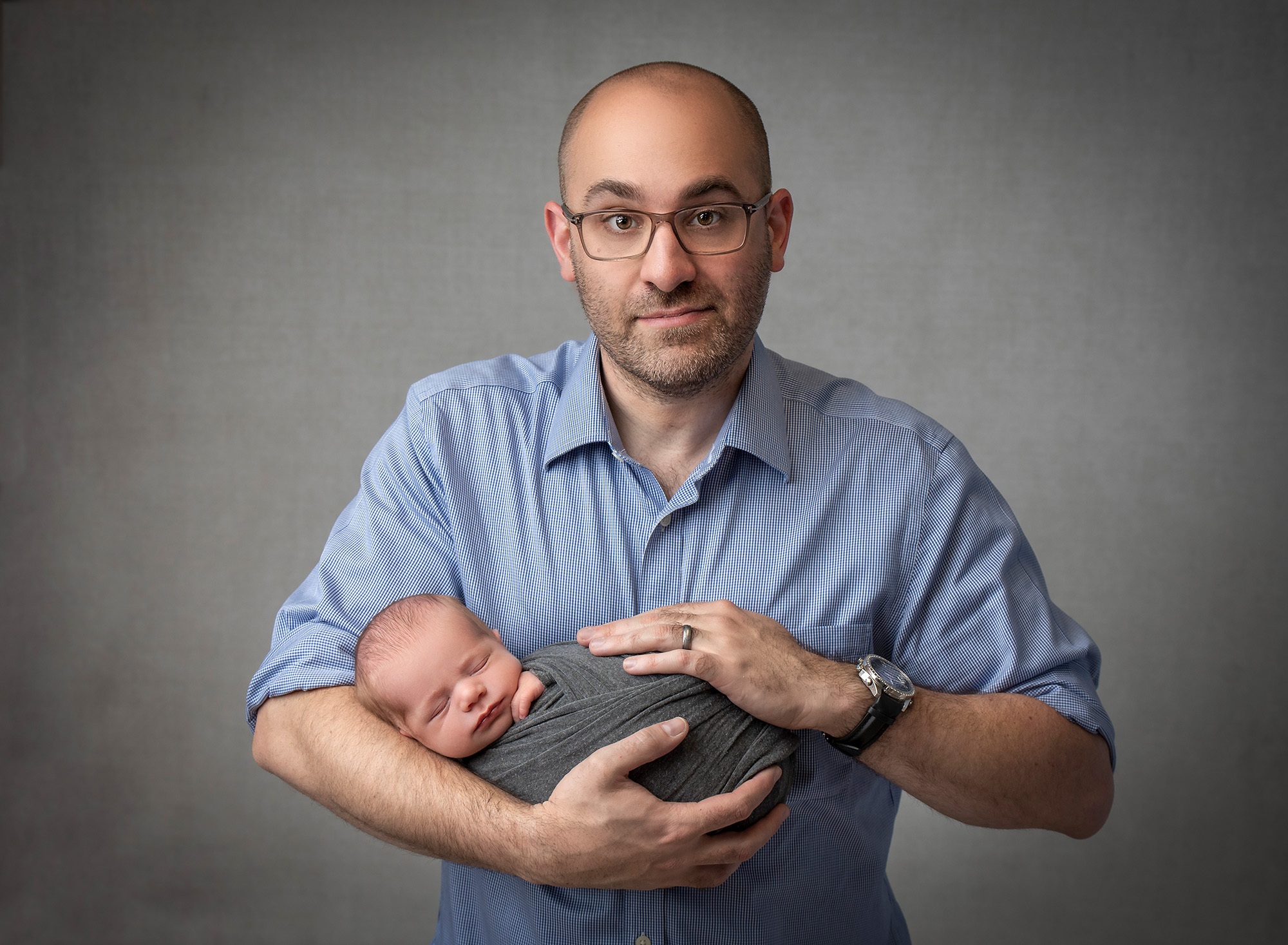 dad cradling newborn baby boy swaddled in gray