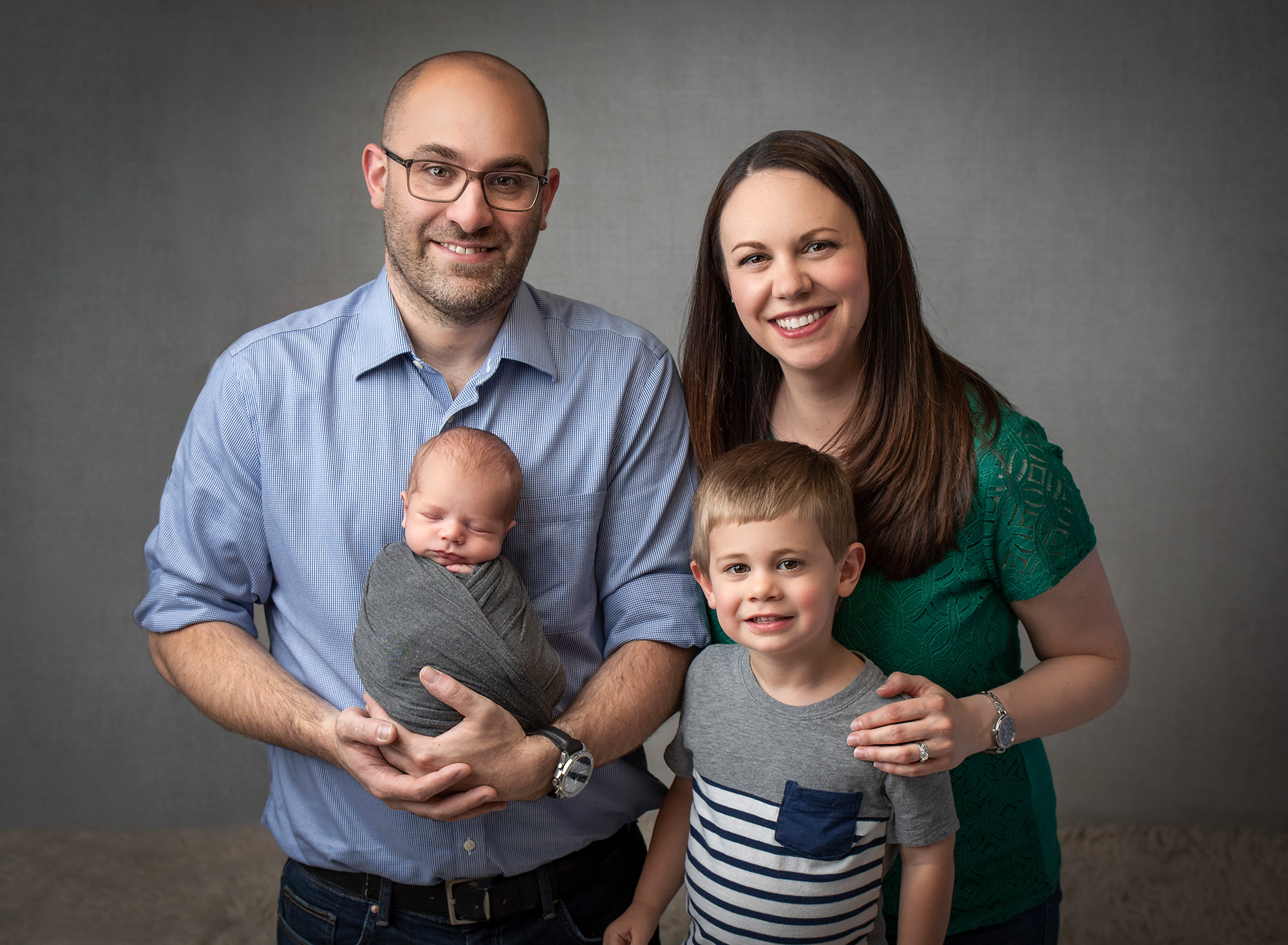 couple posing with young son and newborn baby boy swaddled in gray