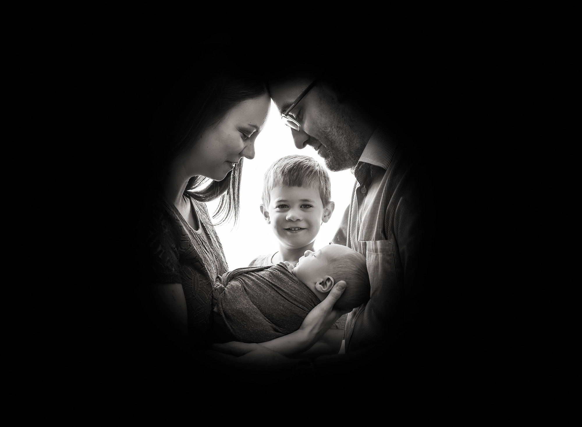 silhouette shadow of parents face's while cradling their newborn baby boy while older son peaks through