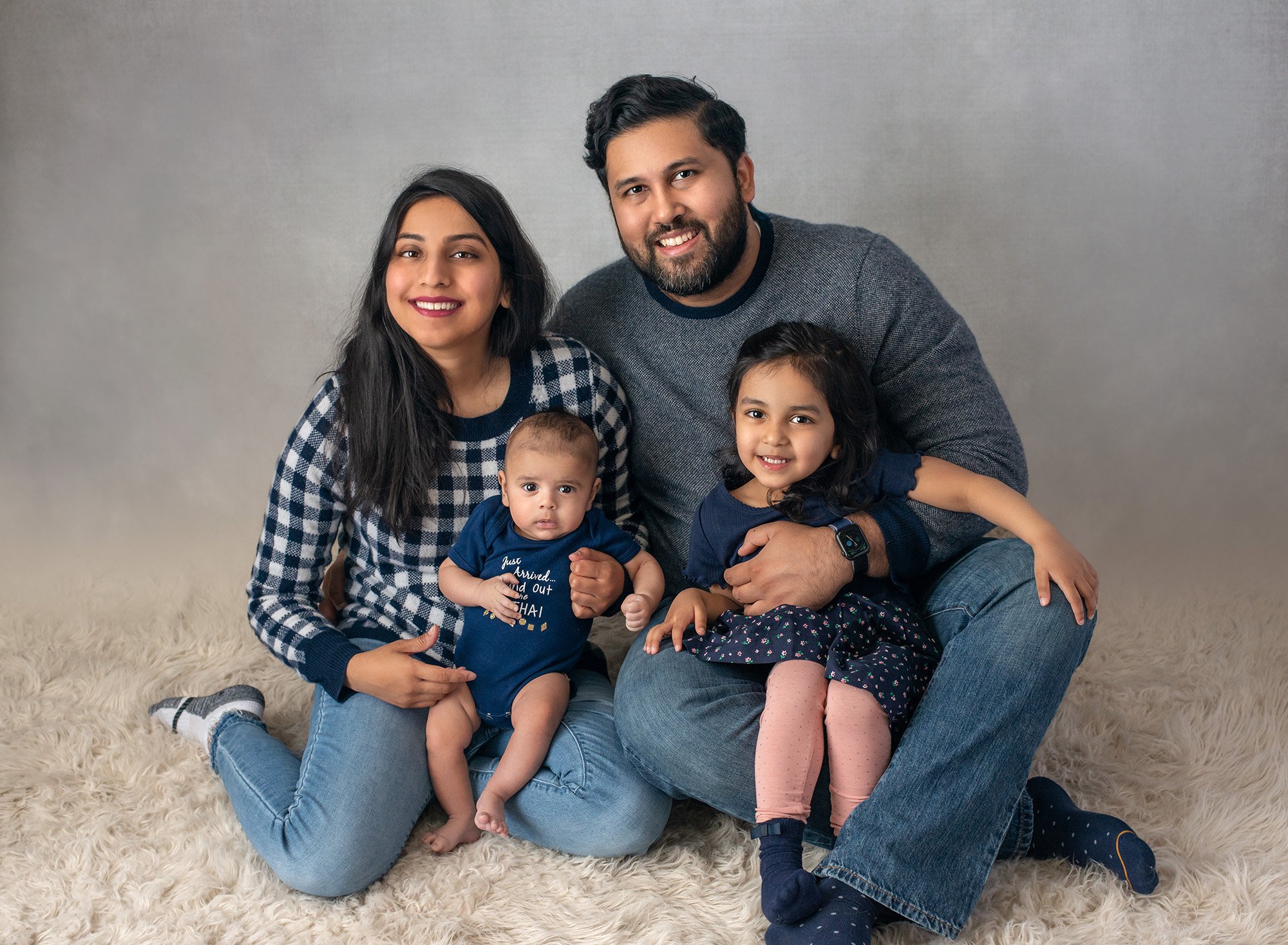 family of 4 posing together wearing navy blue on gray backdrop