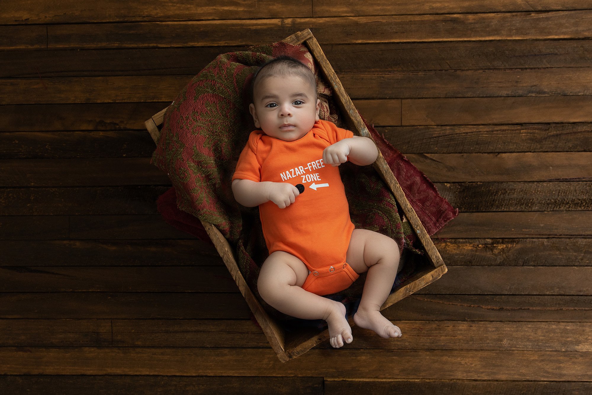 baby portraits newborn boy dressed in orange onesie laying in wooden box