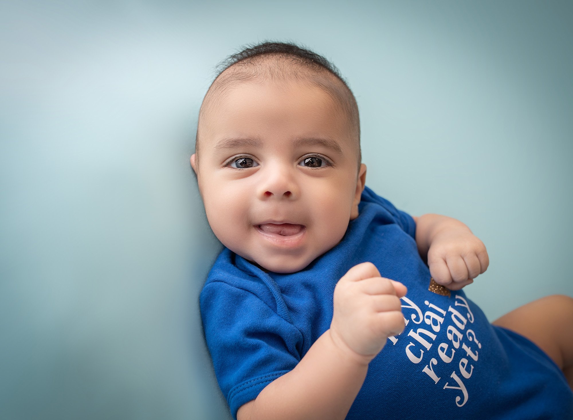 newborn baby boy dressed in royal blue onesie on aqua backdrop