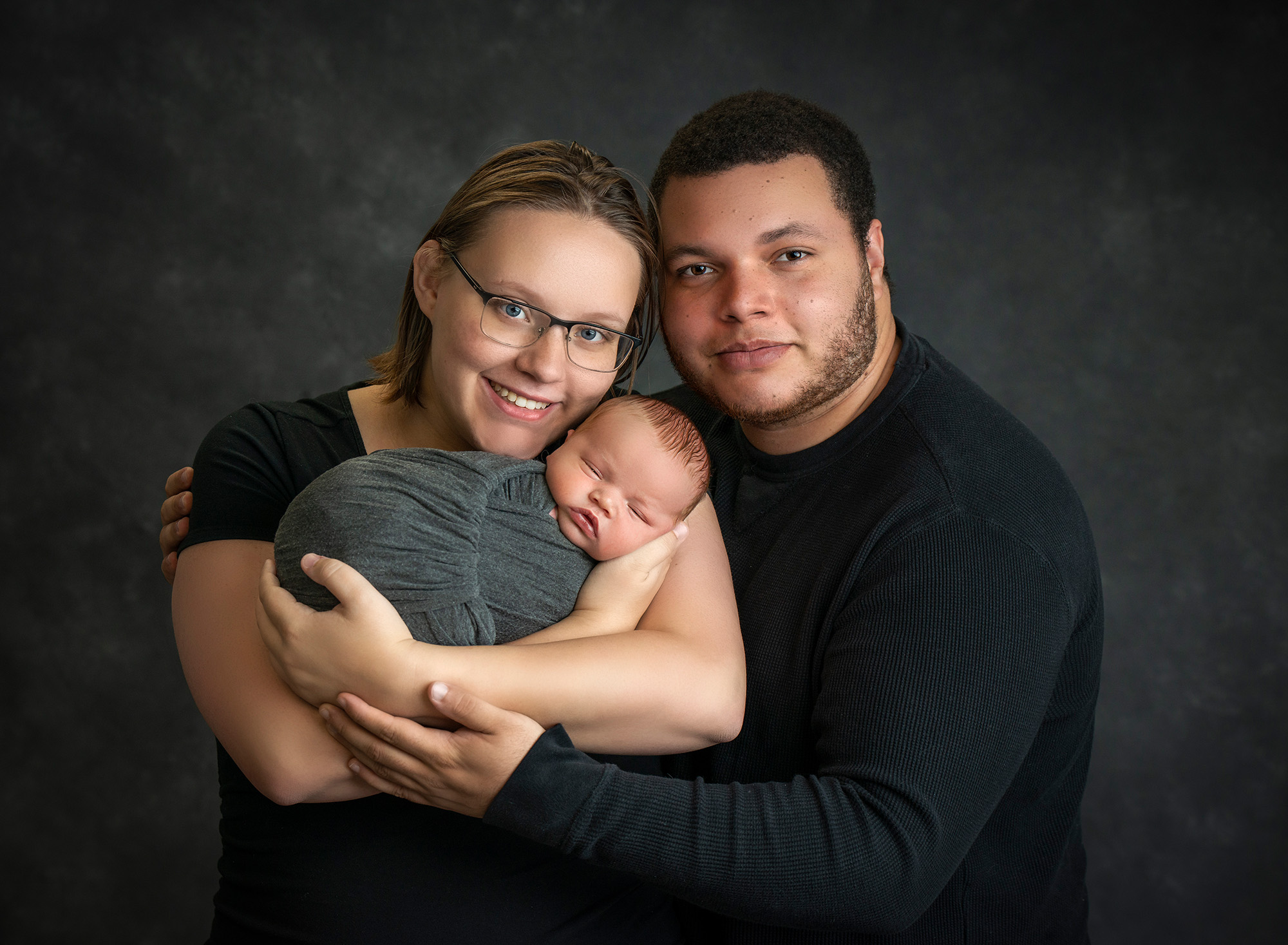 High school sweethearts newborn photos couple posing with newborn baby boy swaddled in gray