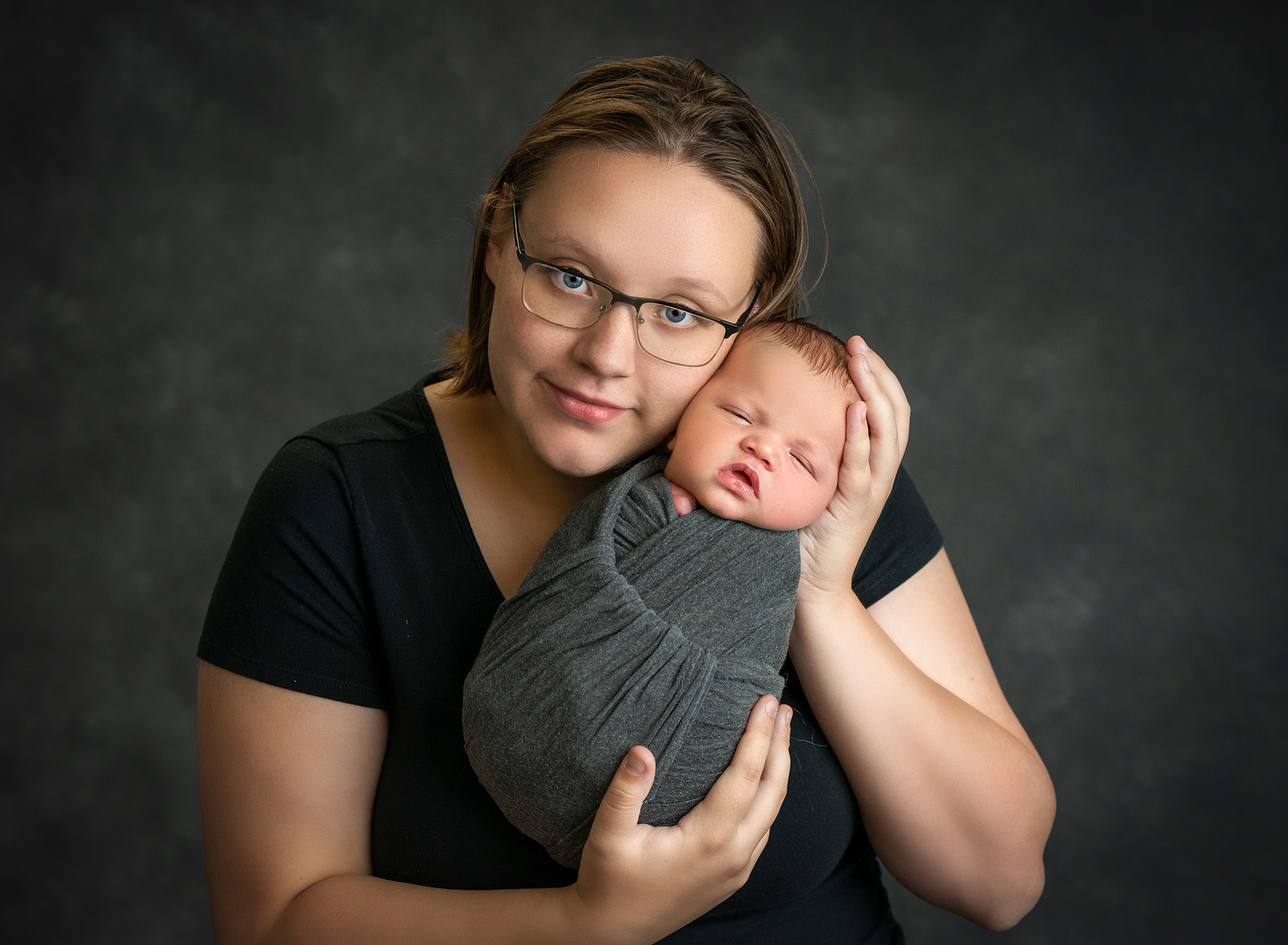 mom cradling newborn baby boy swaddled in gray