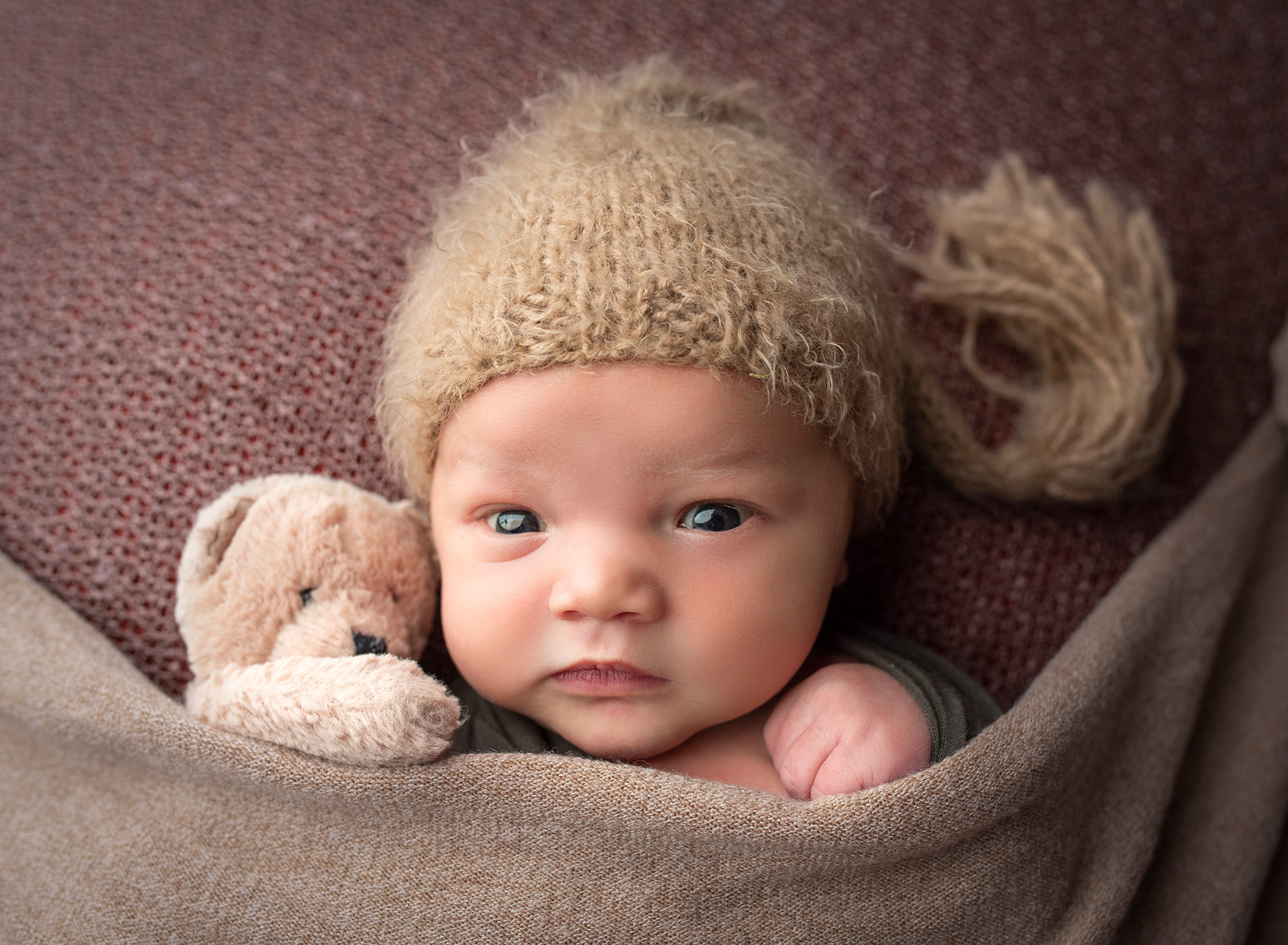 High school sweethearts newborn photos newborn baby boy wide awake wearing brown bonnet tucked in with a teddy bear