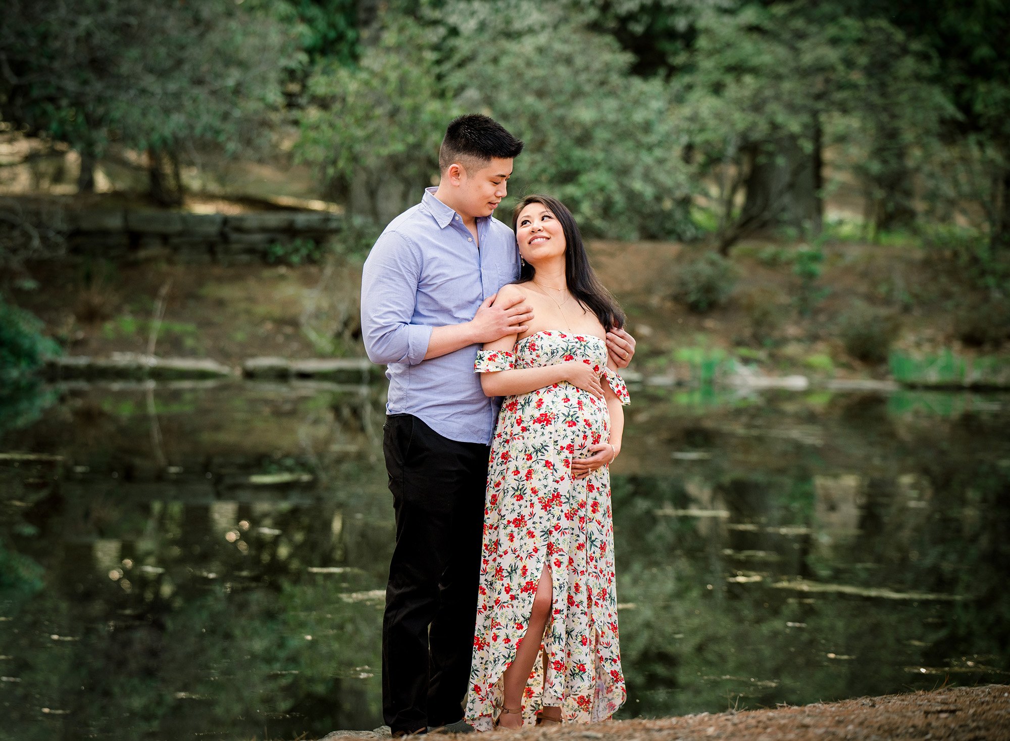 pregnant woman in floral maternity dress posing with partner in front of a pond