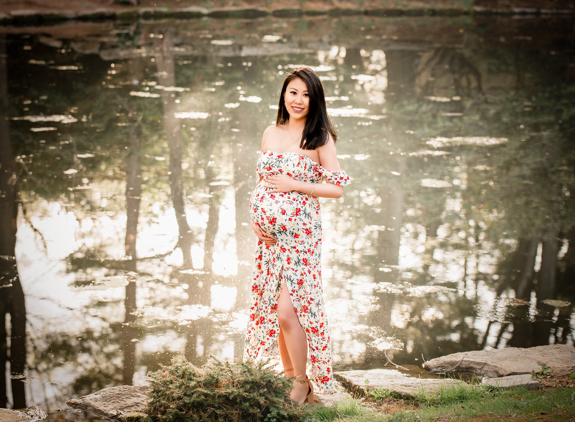 pregnant woman in floral maternity dress standing in front of a pond