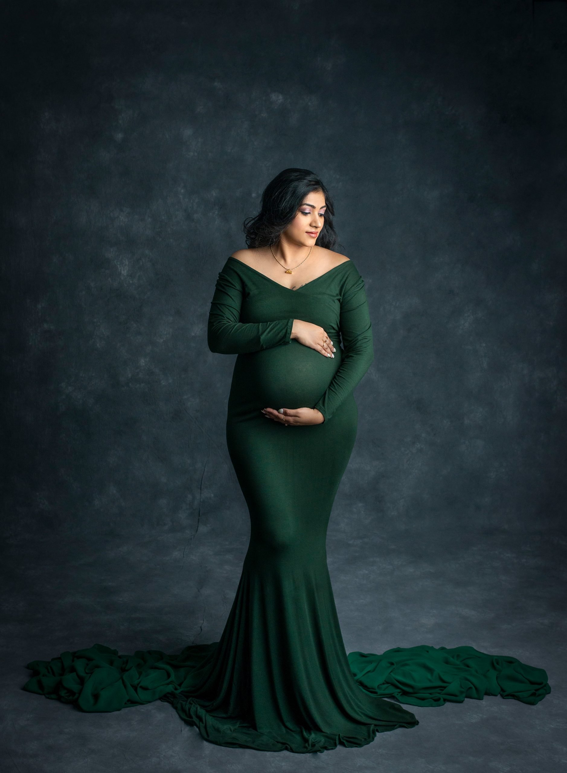 Indian Goddess Maternity photographs pregnant woman posing in green maternity dress with her hands on her pregnant belly