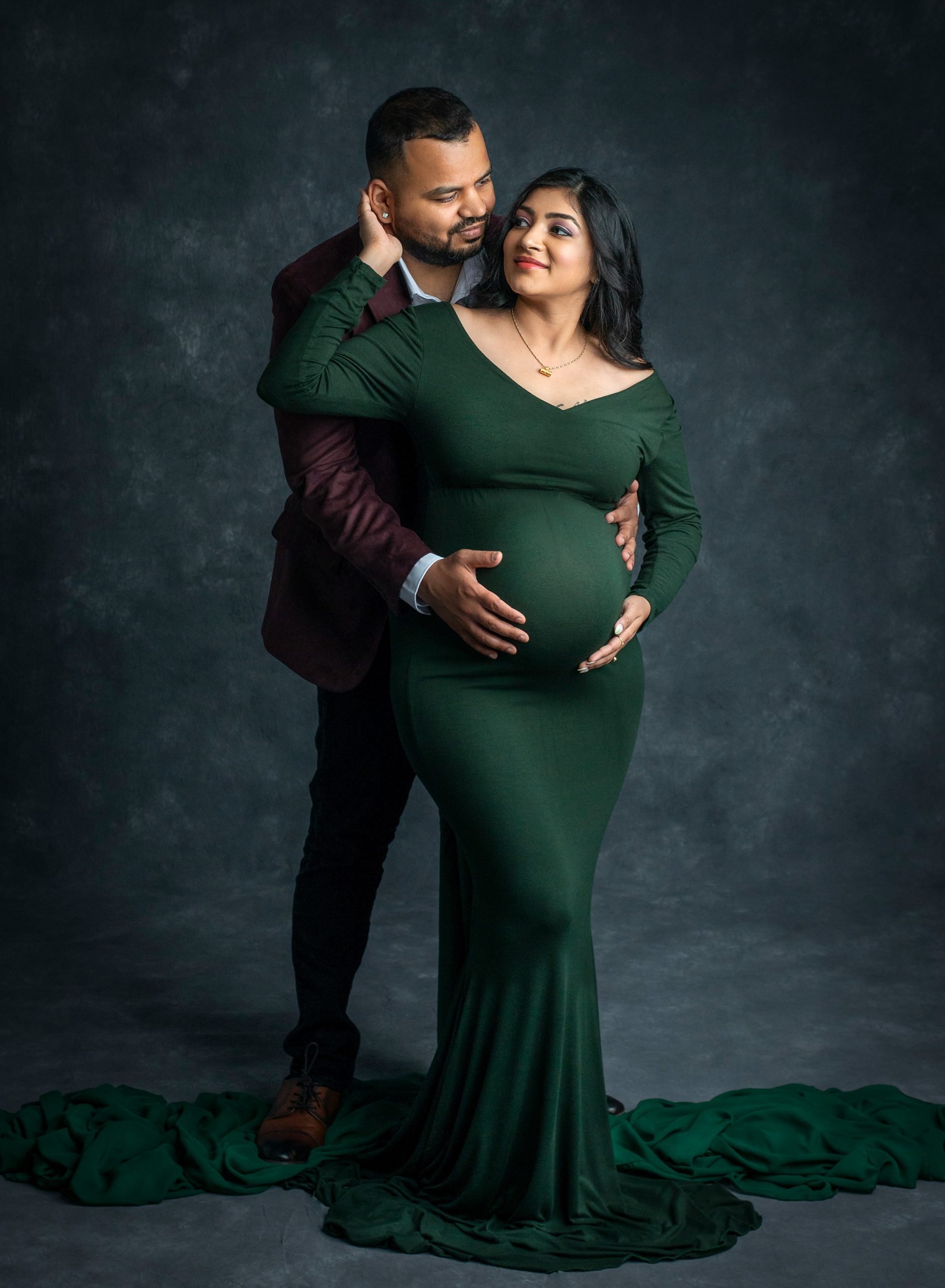 pregnant woman in green dress holding stomach posing with partner