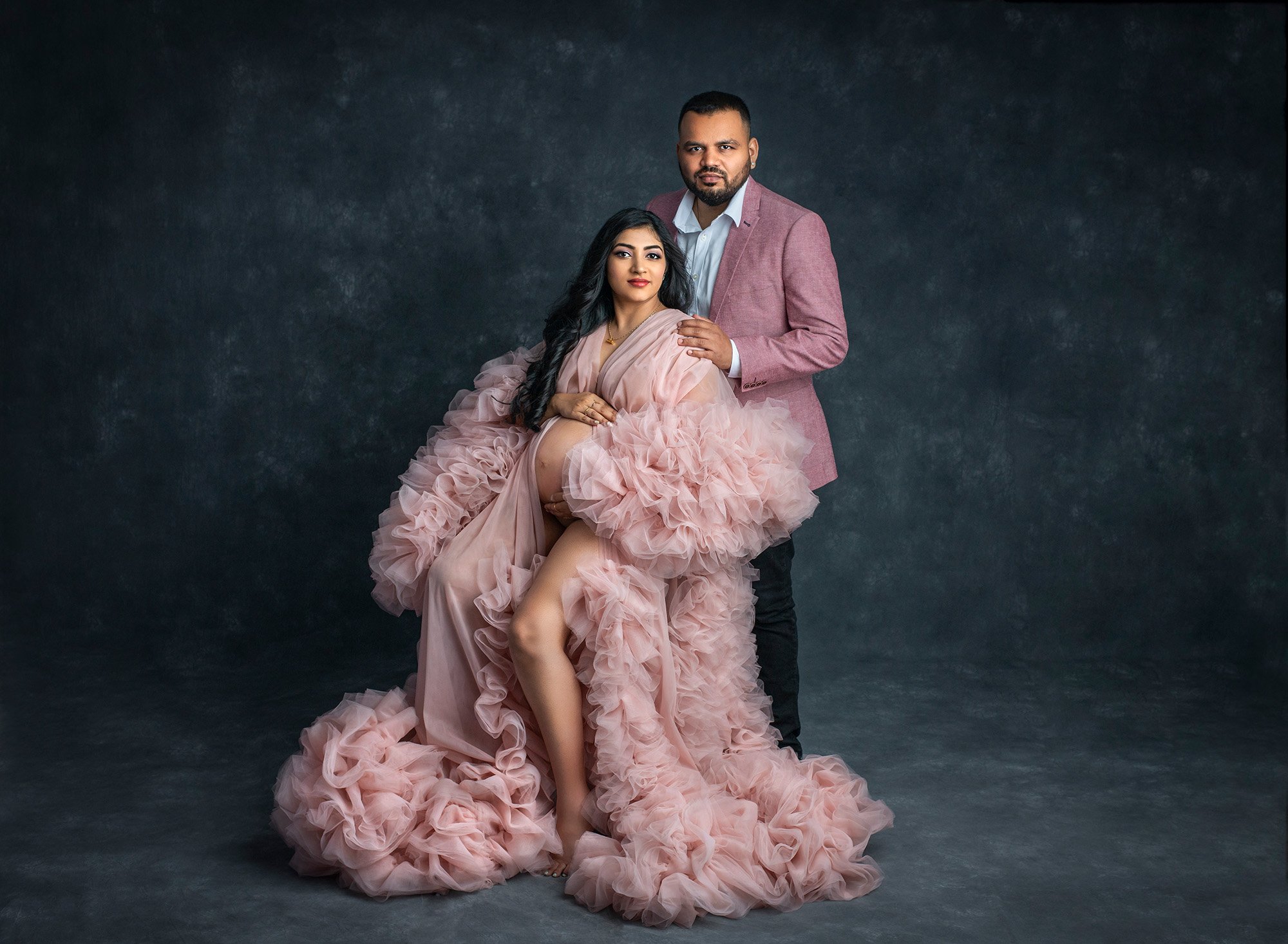 pregnant woman posing with partner wearing ruffled pink dress exposing pregnant stomach