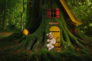 newborn baby boy dressed in bear sweater romper, sitting in front of Winnie the Pooh's tree house