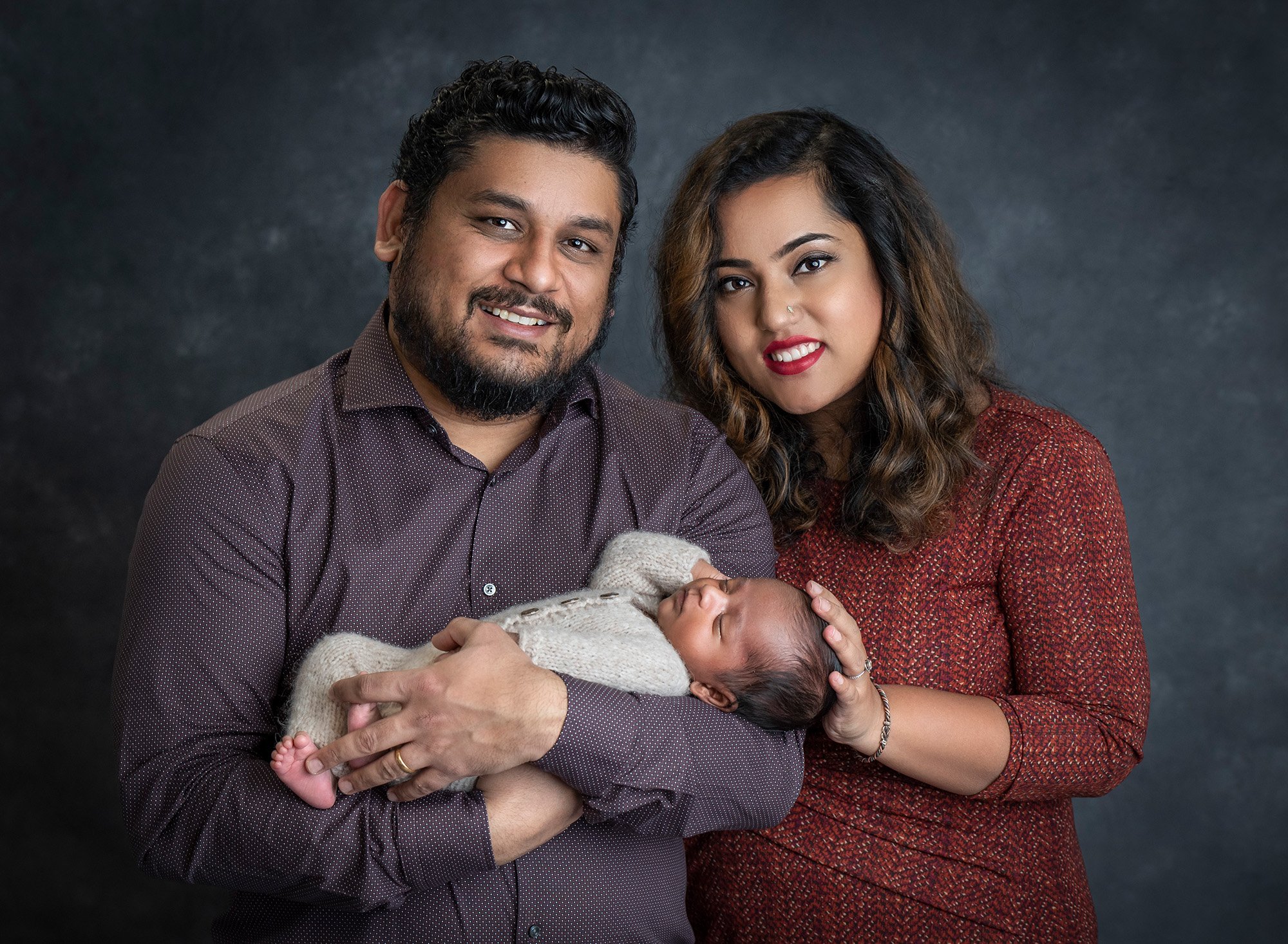 couple posing with newborn baby boy on grey backdrop