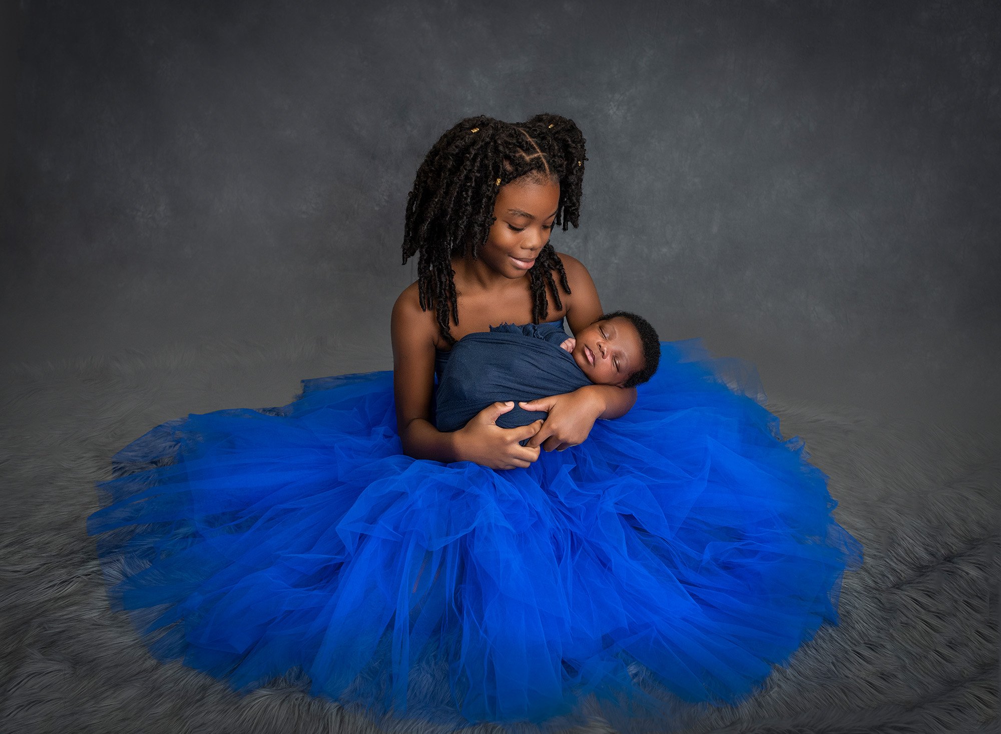 Jamaican boy newborn photographs older sister wearing blue dress cradling newborn baby brother swaddled in blue