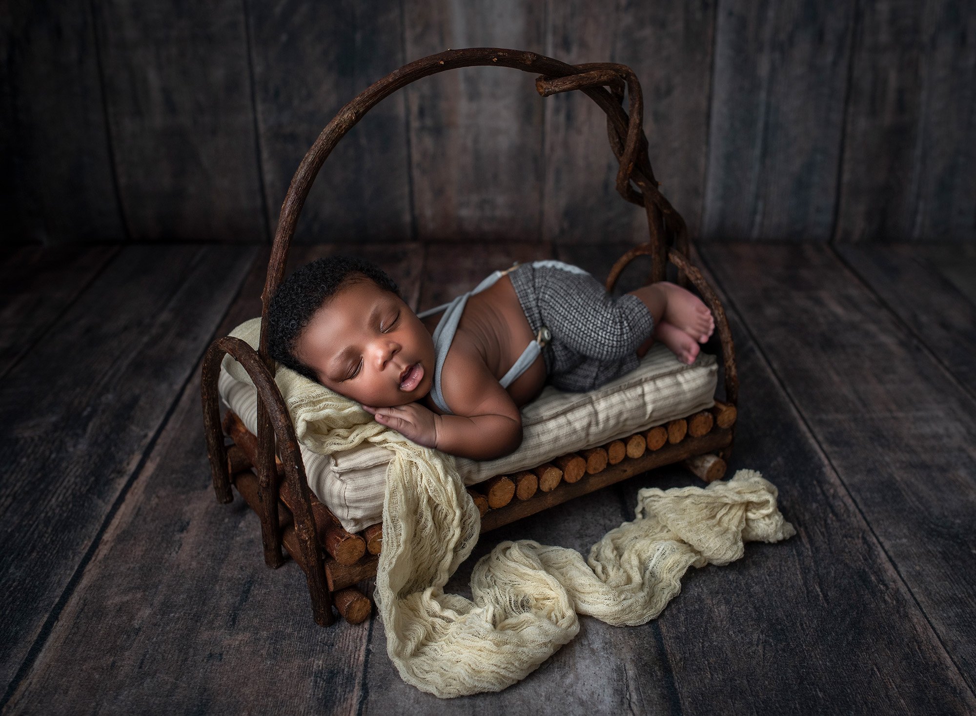 Jamaican boy newborn photographs newborn baby boy asleep in trousers on top of wooden miniature bed