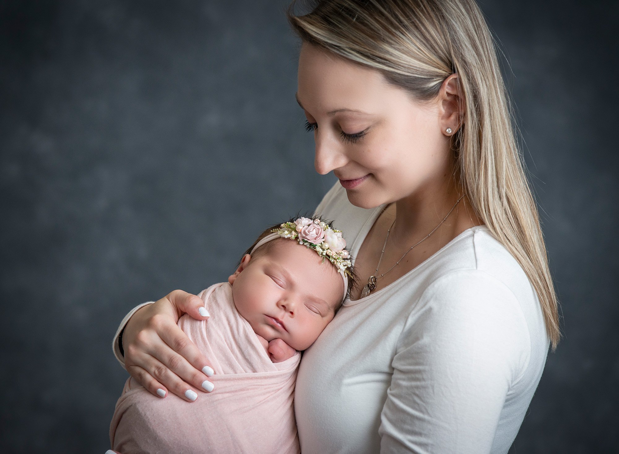 Deployed Military Newborn Photo blonde mother cradling newborn baby girl swaddled in soft pink wearing pink floral headband