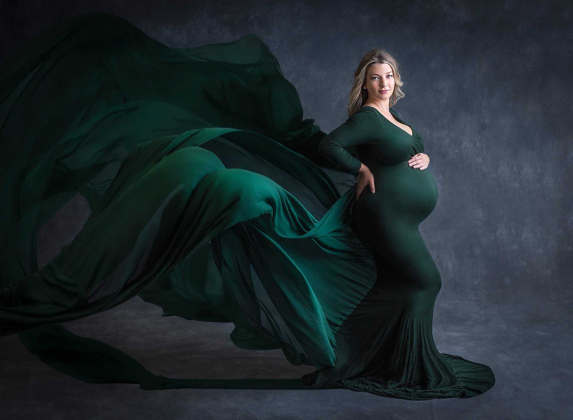 Studio Maternity Photos Glastonbury CT blonde pregnant woman wearing green flowing maternity dress on grey background