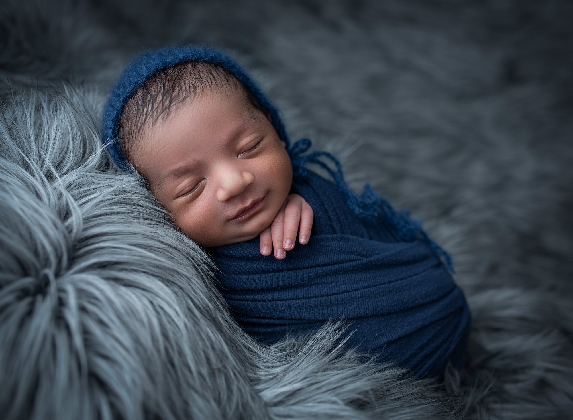 newborn baby boy swaddled in blue sleeping on top of fluffy blanket